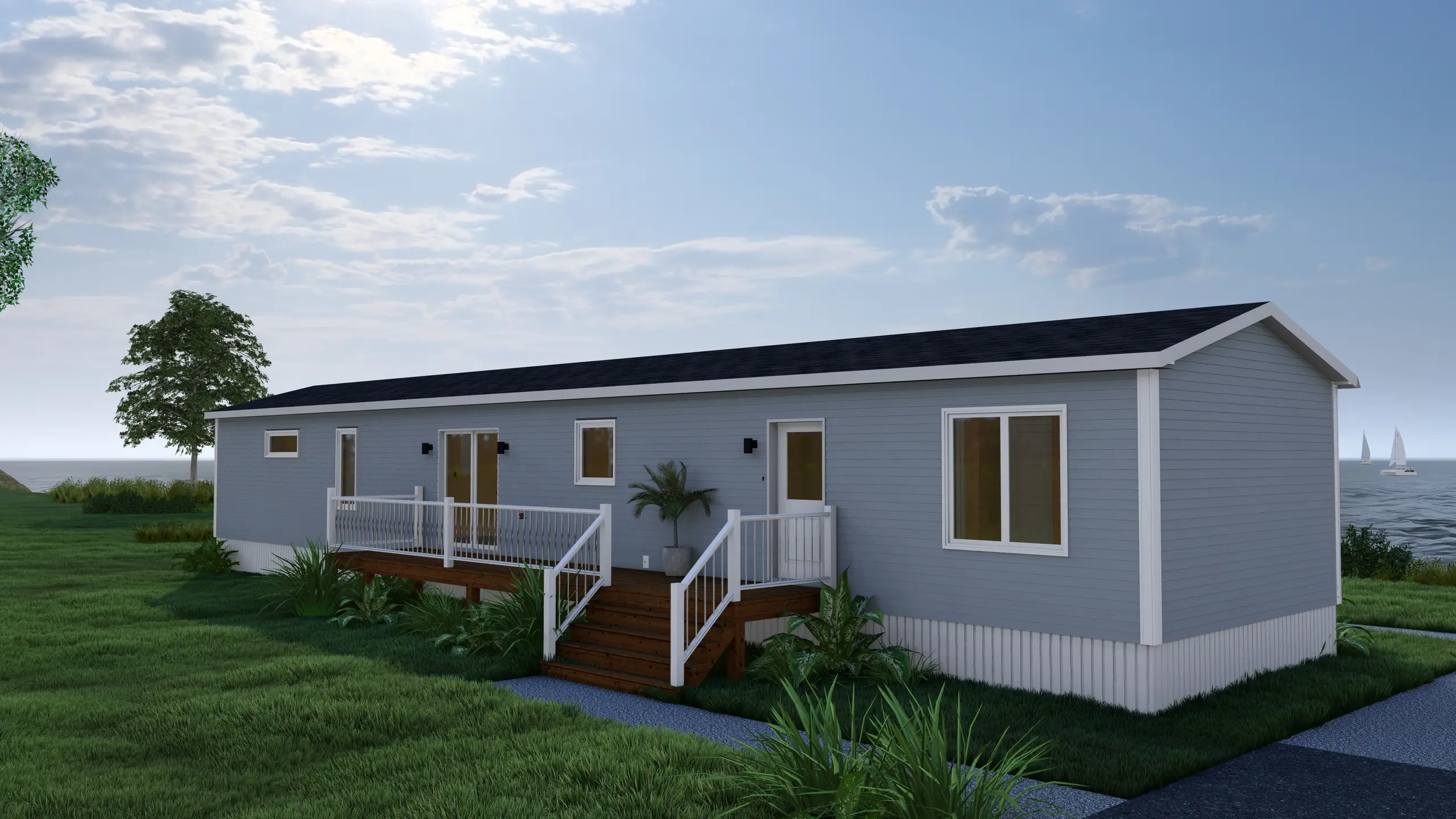 Rear corner view of a coastal mini home featuring a wraparound deck, sliding patio doors, light grey siding, and ocean views in the background. 