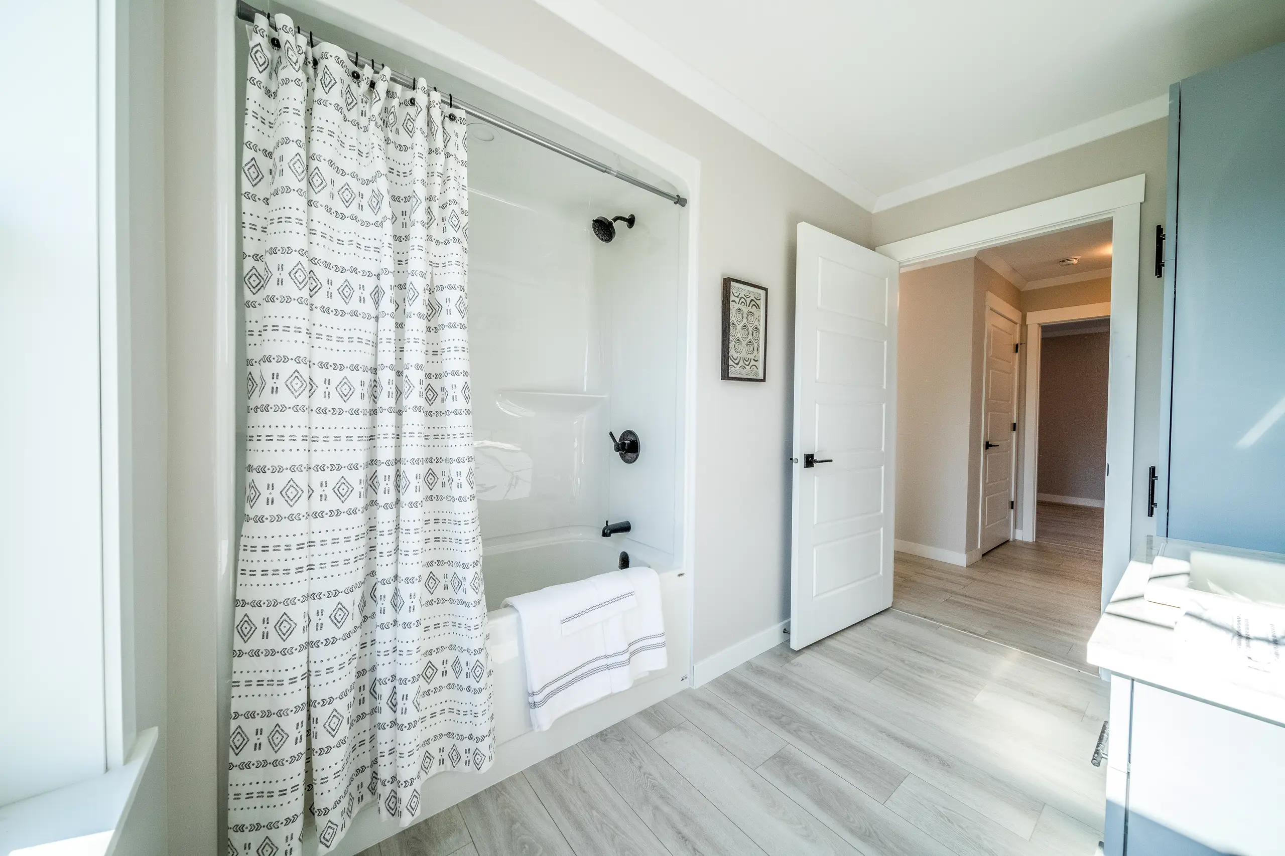 Clean, modern bathroom with a tub-shower combination, patterned shower curtain, light flooring, and neutral finishes. 