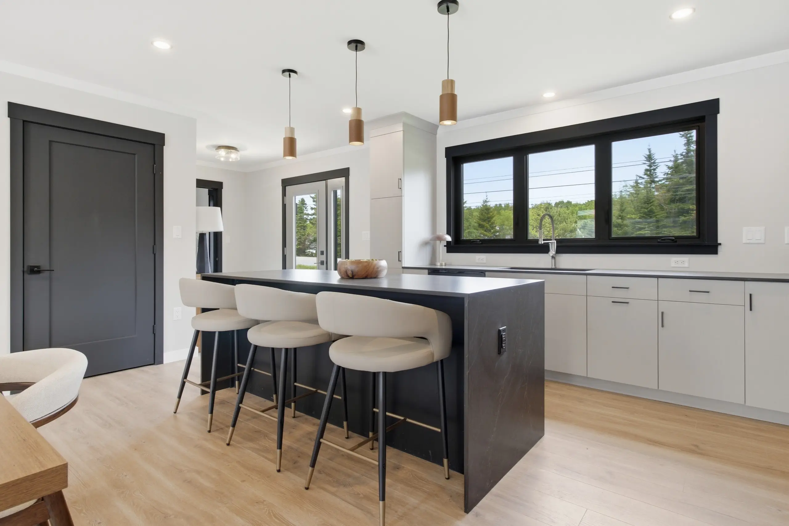 Modern kitchen with a large island, seating for four, sleek cabinetry, pendant lighting, and expansive windows overlooking the outdoors. 