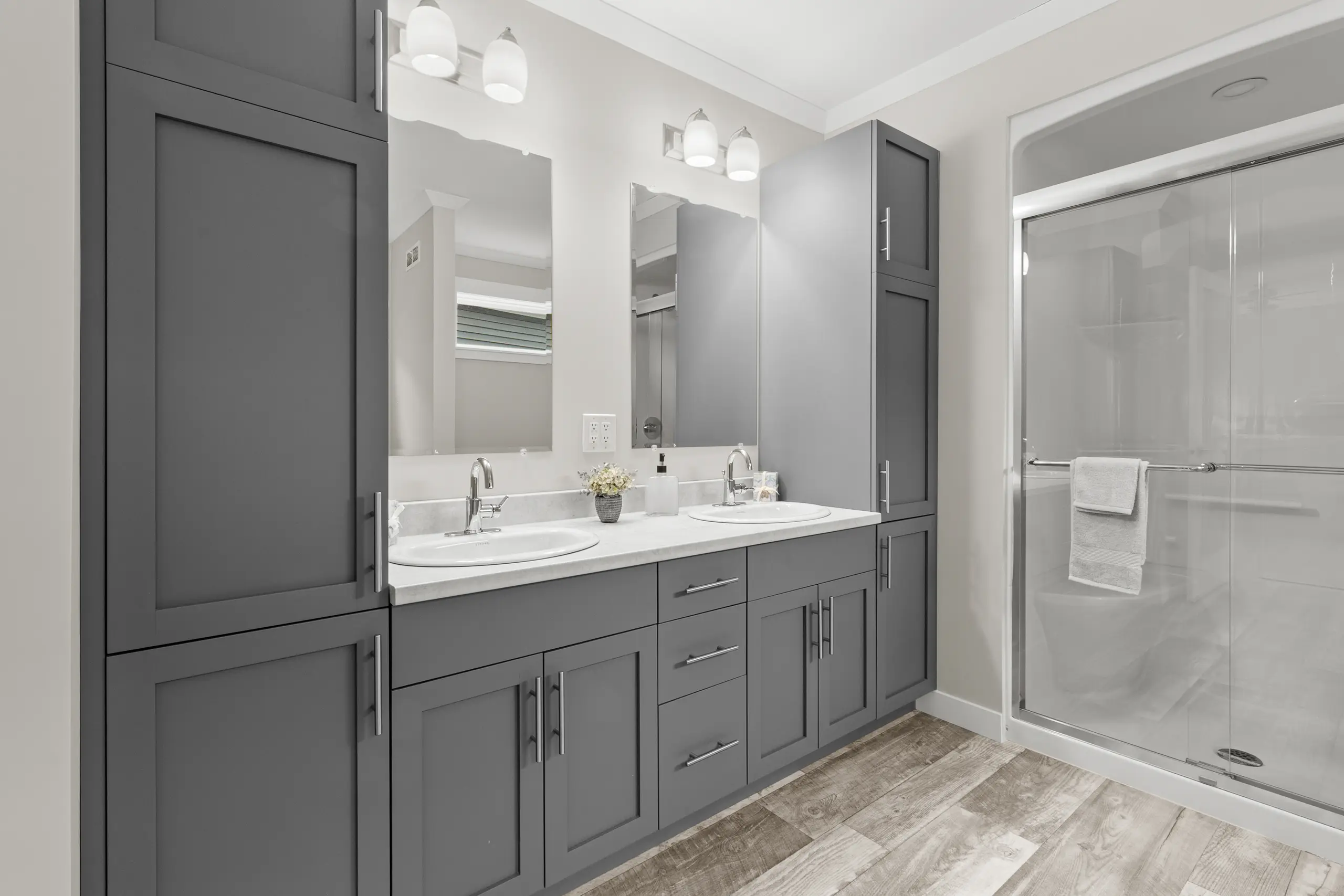 Ensuite bathroom with double vanity, grey cabinetry, ample storage, and a glass-enclosed shower. 
