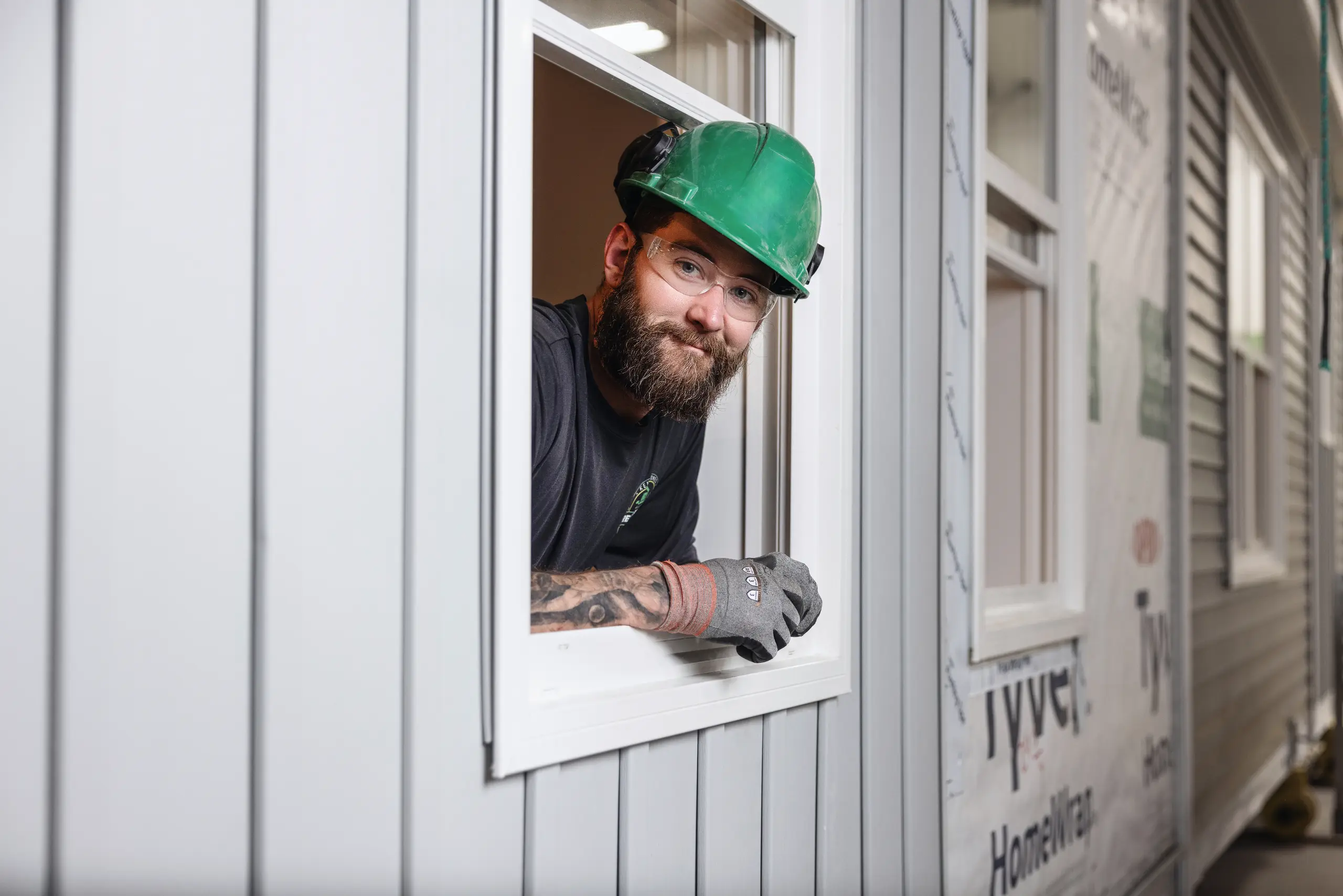 Kent Homes Dream Builder wearing a hard hat and gloves, leaning through a window opening during modular home construction. 