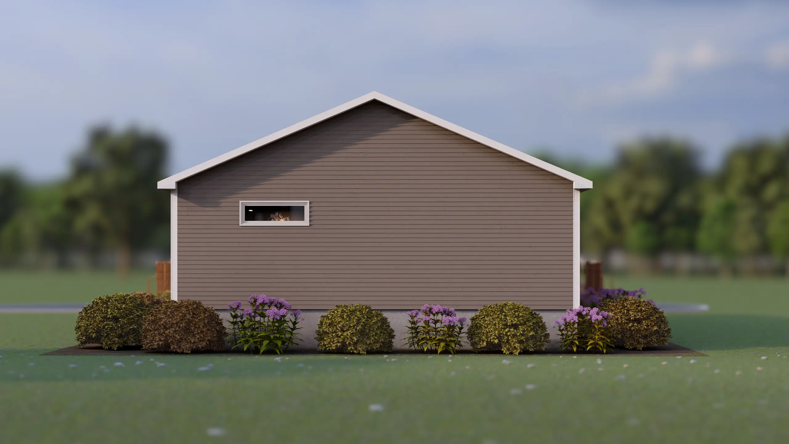 Side elevation of a modular home with a simple grey exterior, a narrow horizontal window, and a row of shrubs and flowering plants along the foundation. 