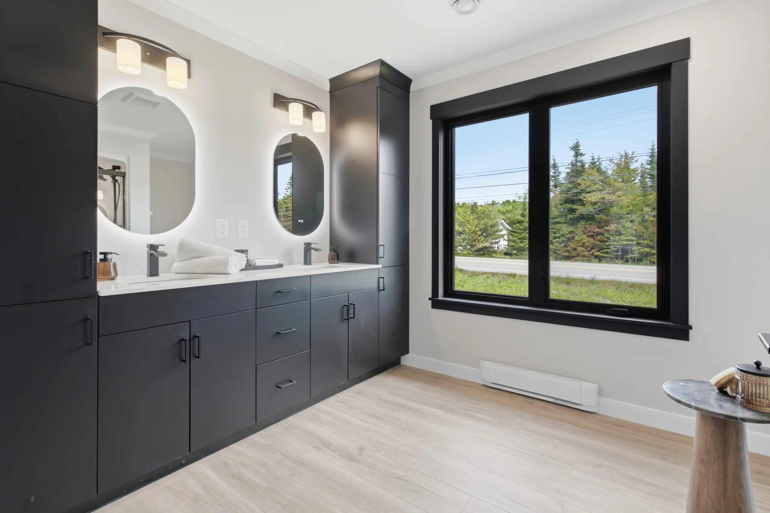Modern ensuite bathroom featuring a double vanity, large storage cabinets, contemporary lighting, and a spacious window. 
