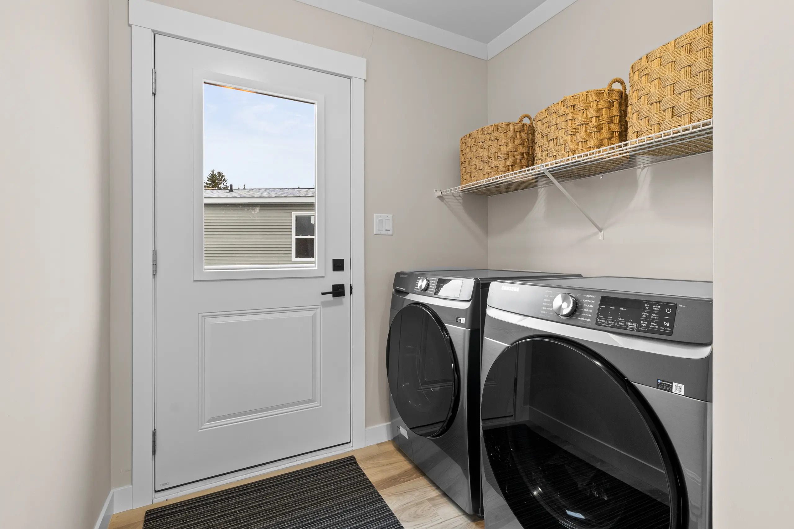 Functional laundry room with front-loading washer and dryer, overhead storage shelving, and an exterior access door. 