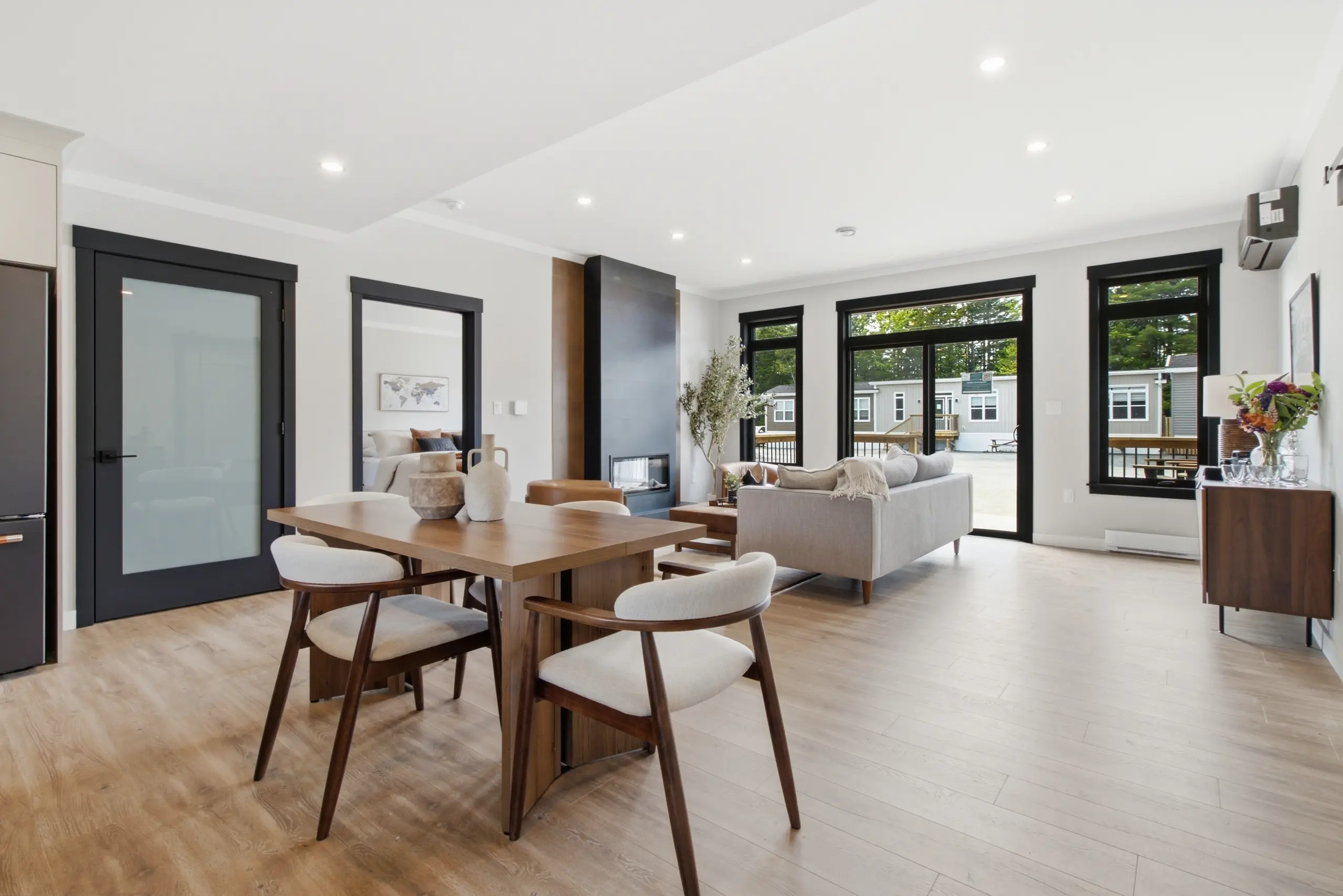 Open-concept dining and living area with large windows, modern furnishings, a cozy fireplace, and abundant natural light. 