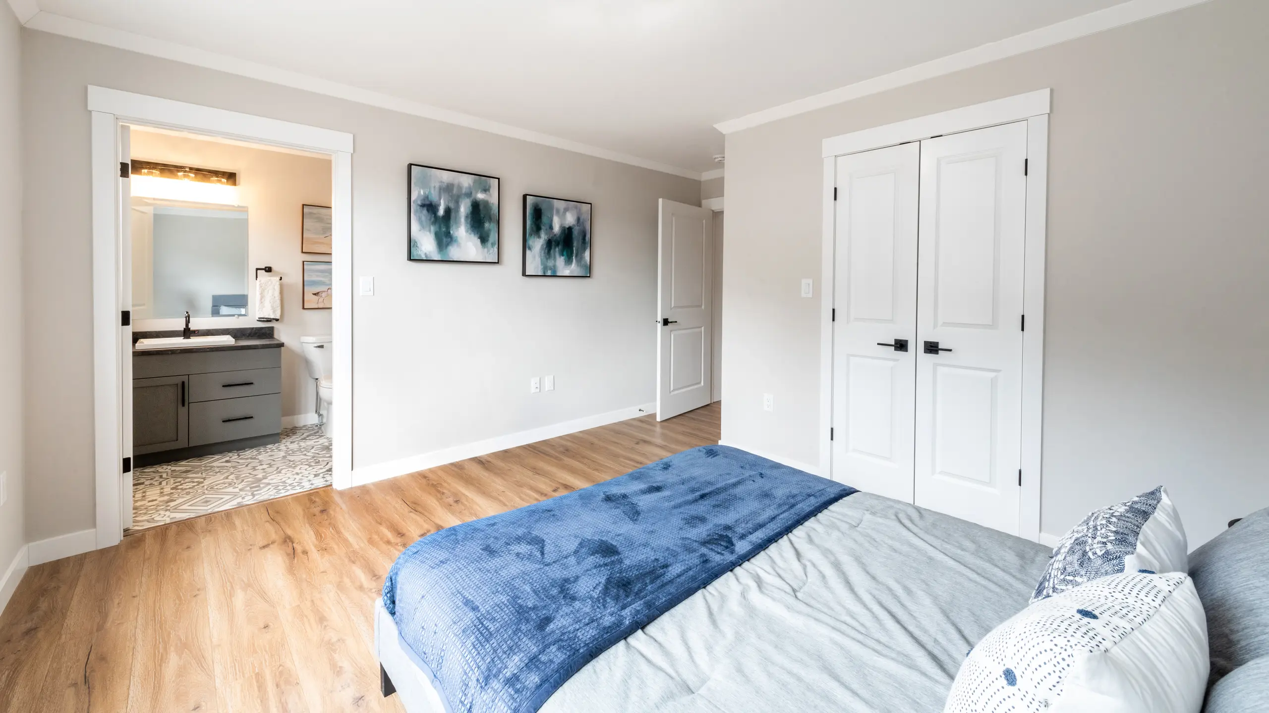 Bedroom with a queen bed and blue bedding, featuring an open doorway leading to an ensuite bathroom. 
