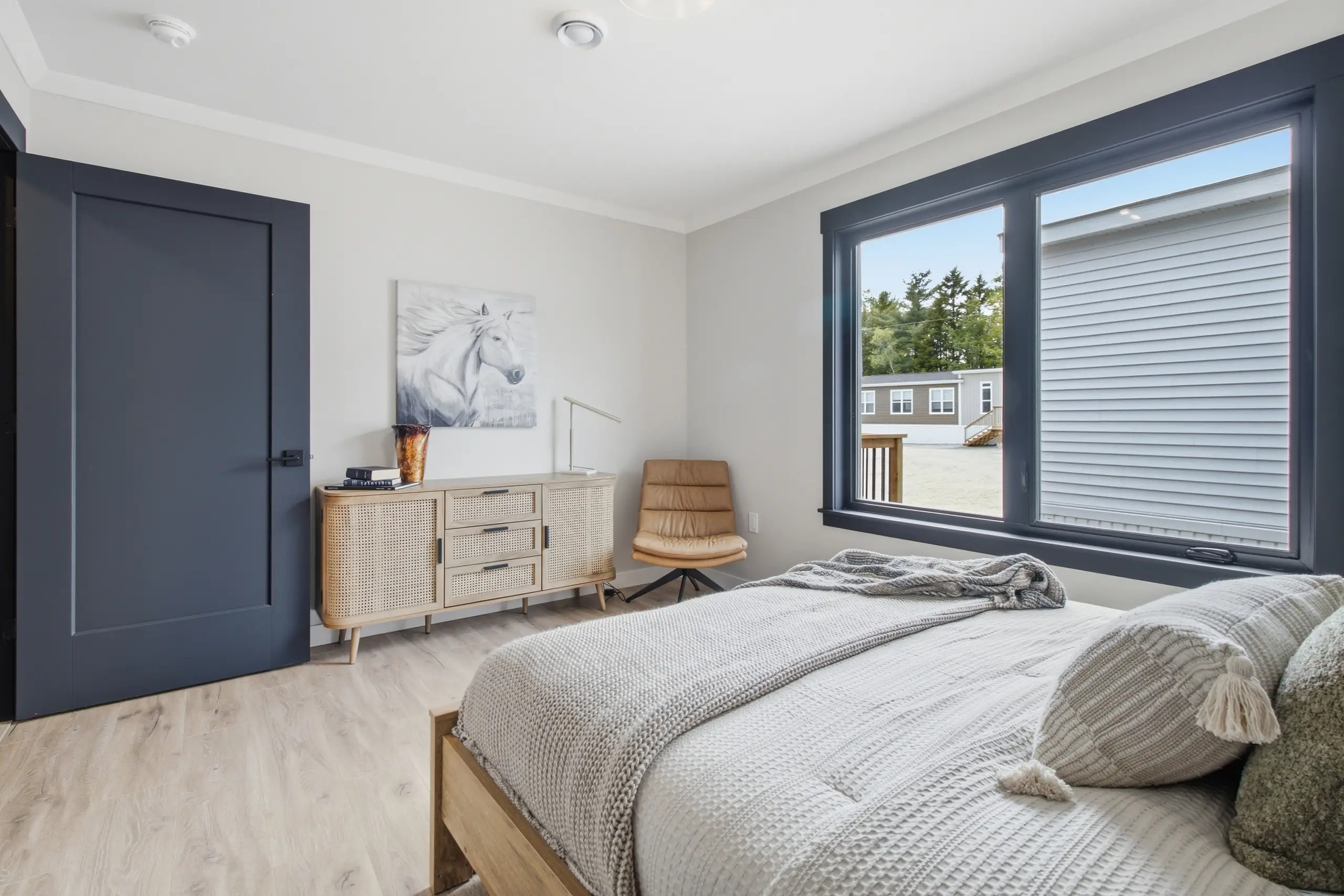 Contemporary bedroom featuring a large picture window, warm wood furnishings, neutral décor, and a comfortable sleeping space. 
