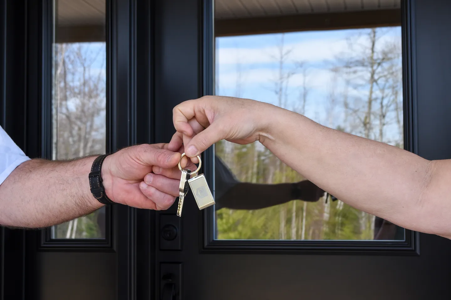 Close-up of two hands exchanging a set of house keys in front of a modern black front door with large glass panels, marking the moment of move-in at a new Kent Homes residence 