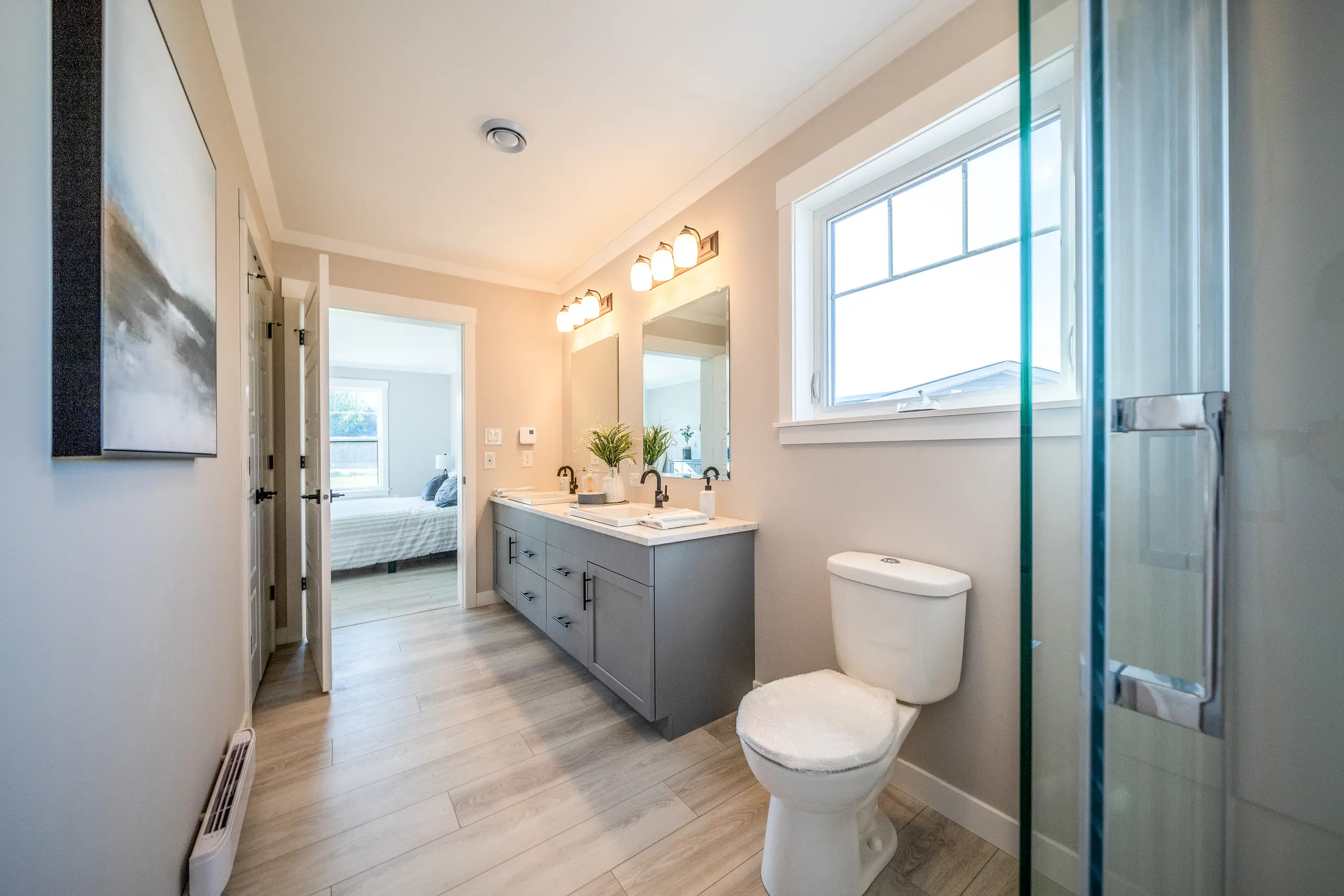 Modern ensuite bathroom with double vanity, glass shower, large window, and bright, contemporary finishes. 