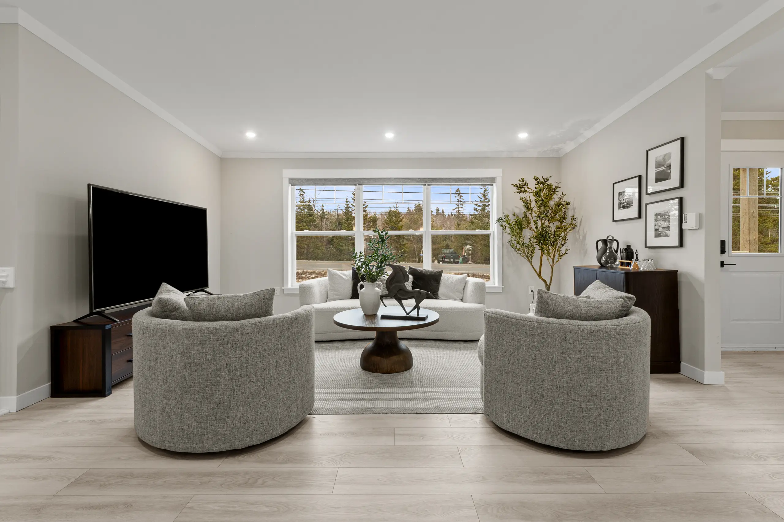 Bright living room featuring a white sofa, two accent chairs, large front window, and modern neutral décor. 