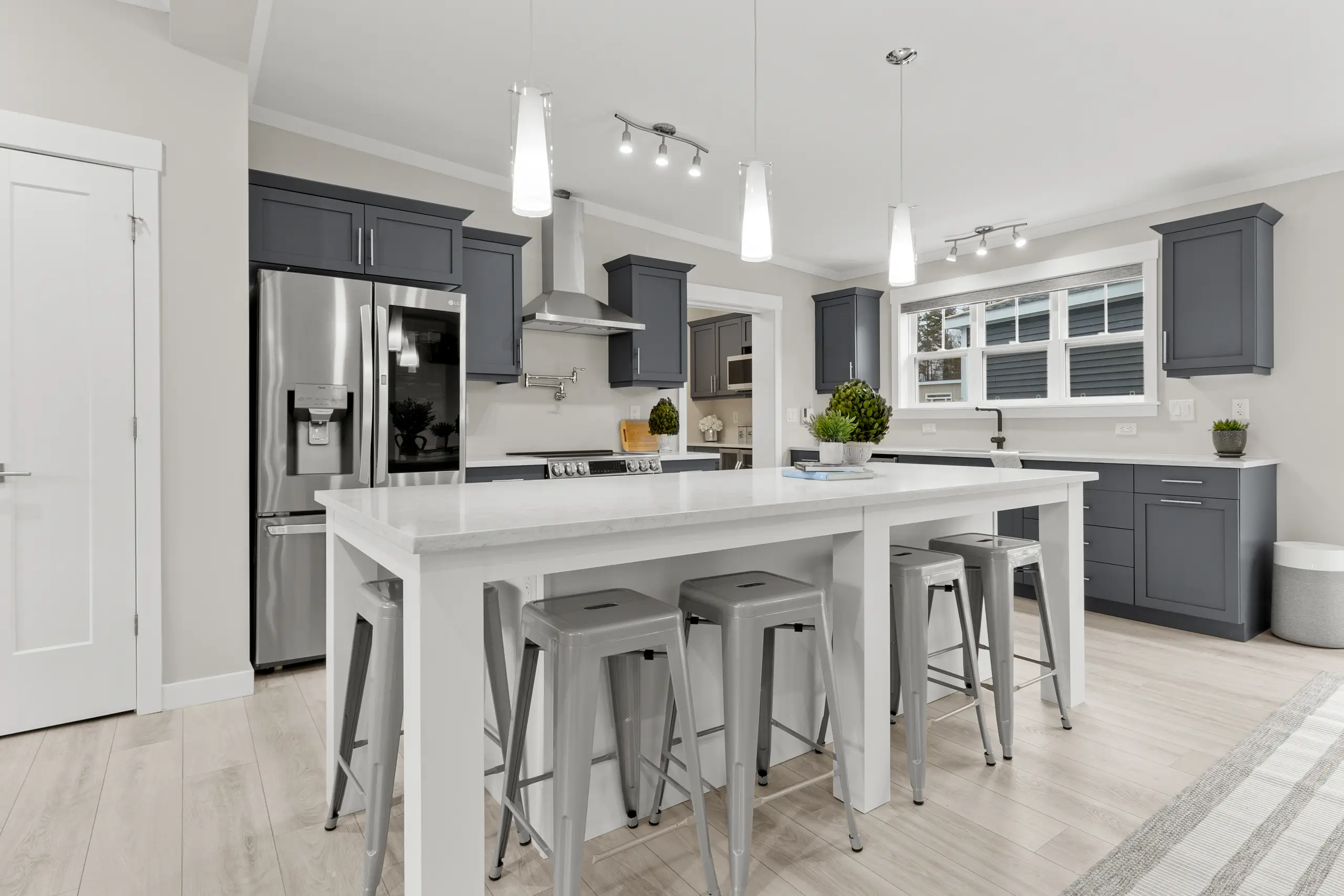 Modern kitchen with grey shaker cabinets, stainless steel appliances, large island seating, and white quartz-style countertops. 