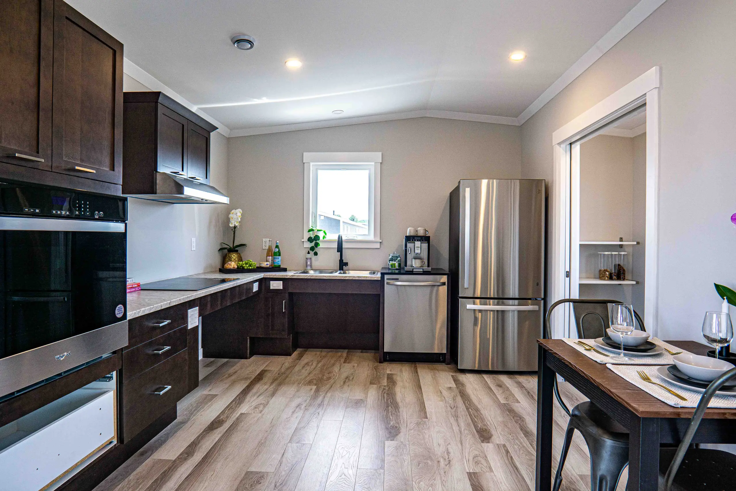 Bright L-shaped kitchen featuring dark cabinetry, stainless steel appliances, ample counter space, and an adjacent dining area with pantry access. 