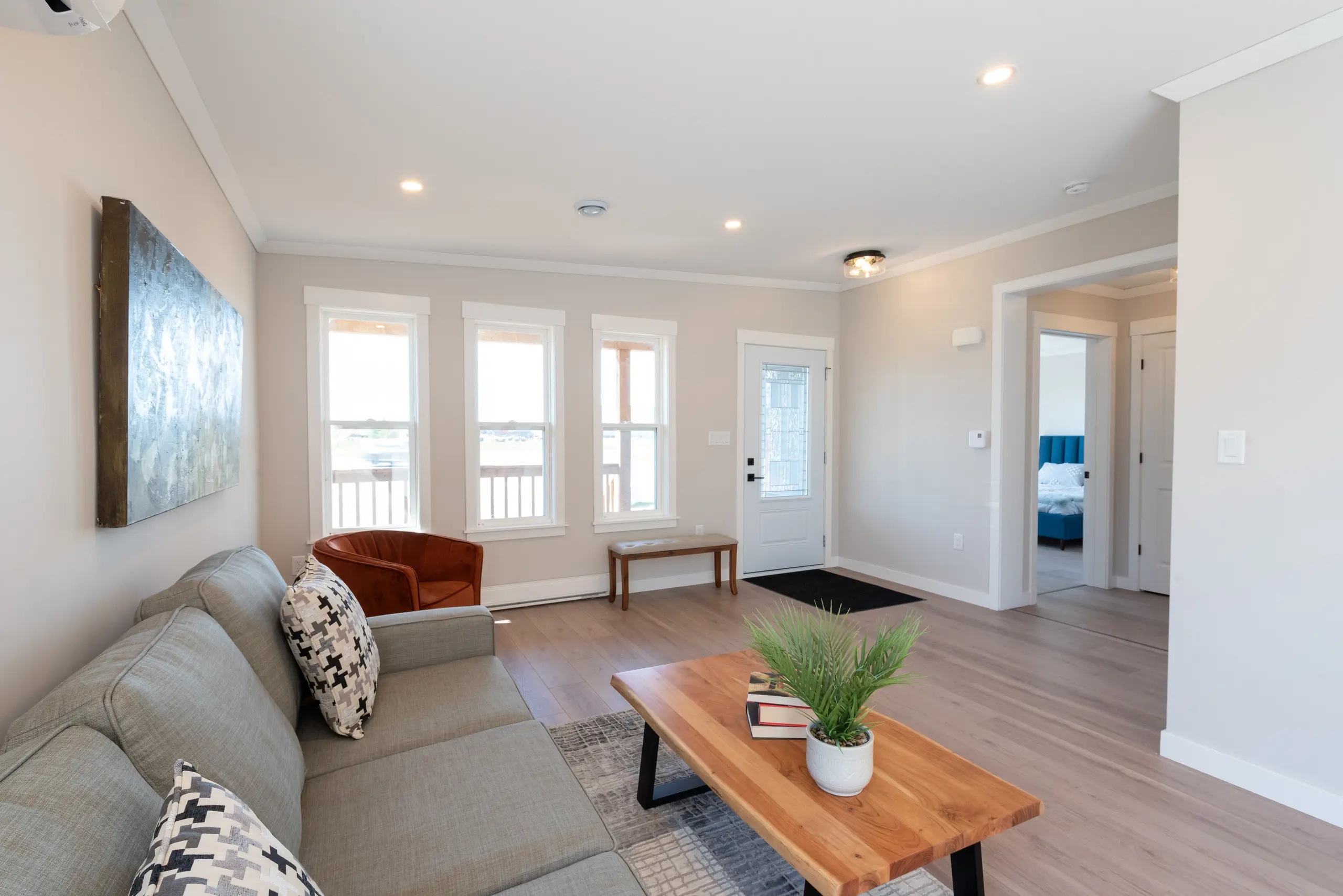 Spacious living room featuring large windows, a neutral sofa, accent chair, wood coffee table, and abundant natural light. 