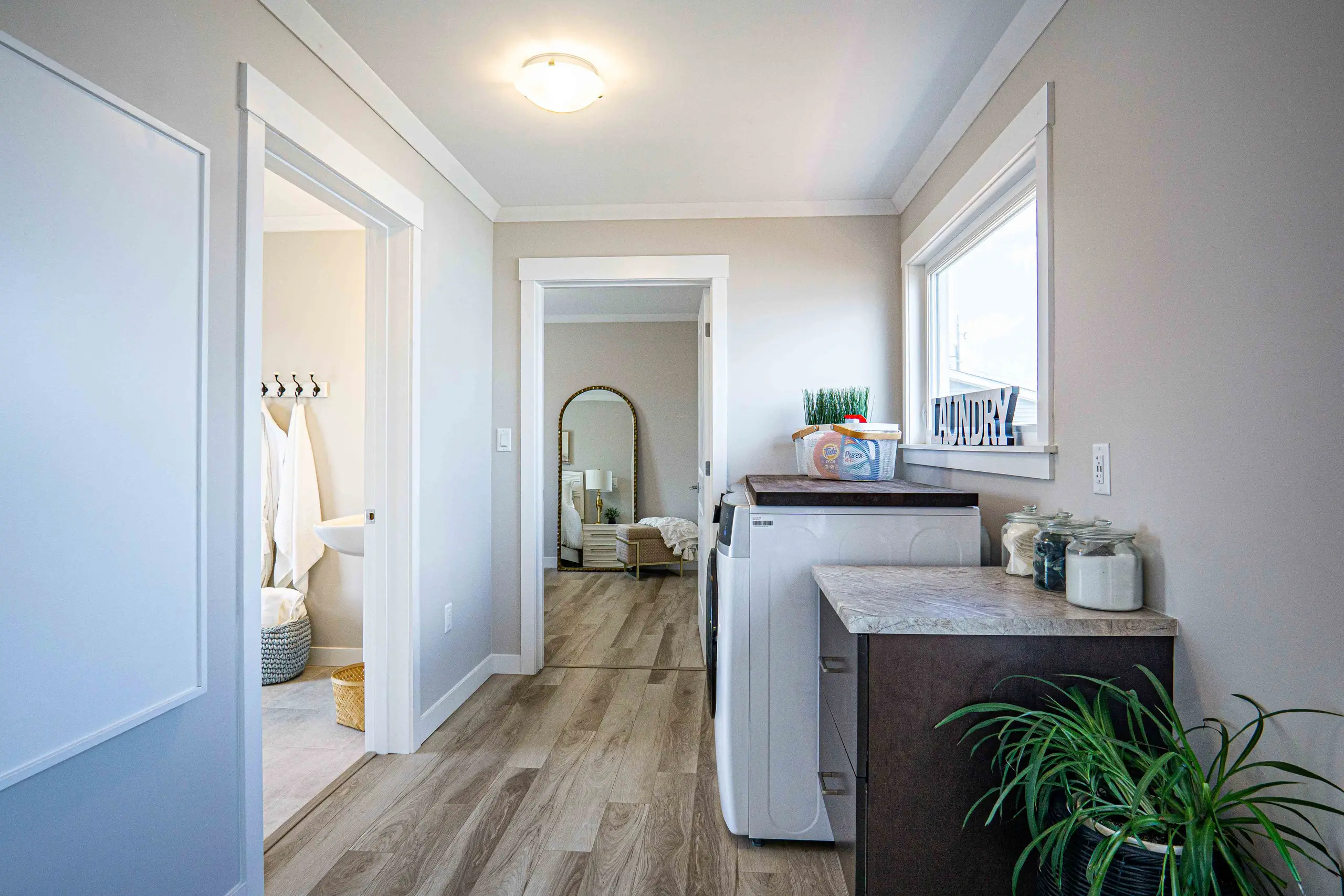 Functional laundry room with full-size washer and dryer, storage cabinetry, countertop workspace, and direct access to adjacent rooms. 
