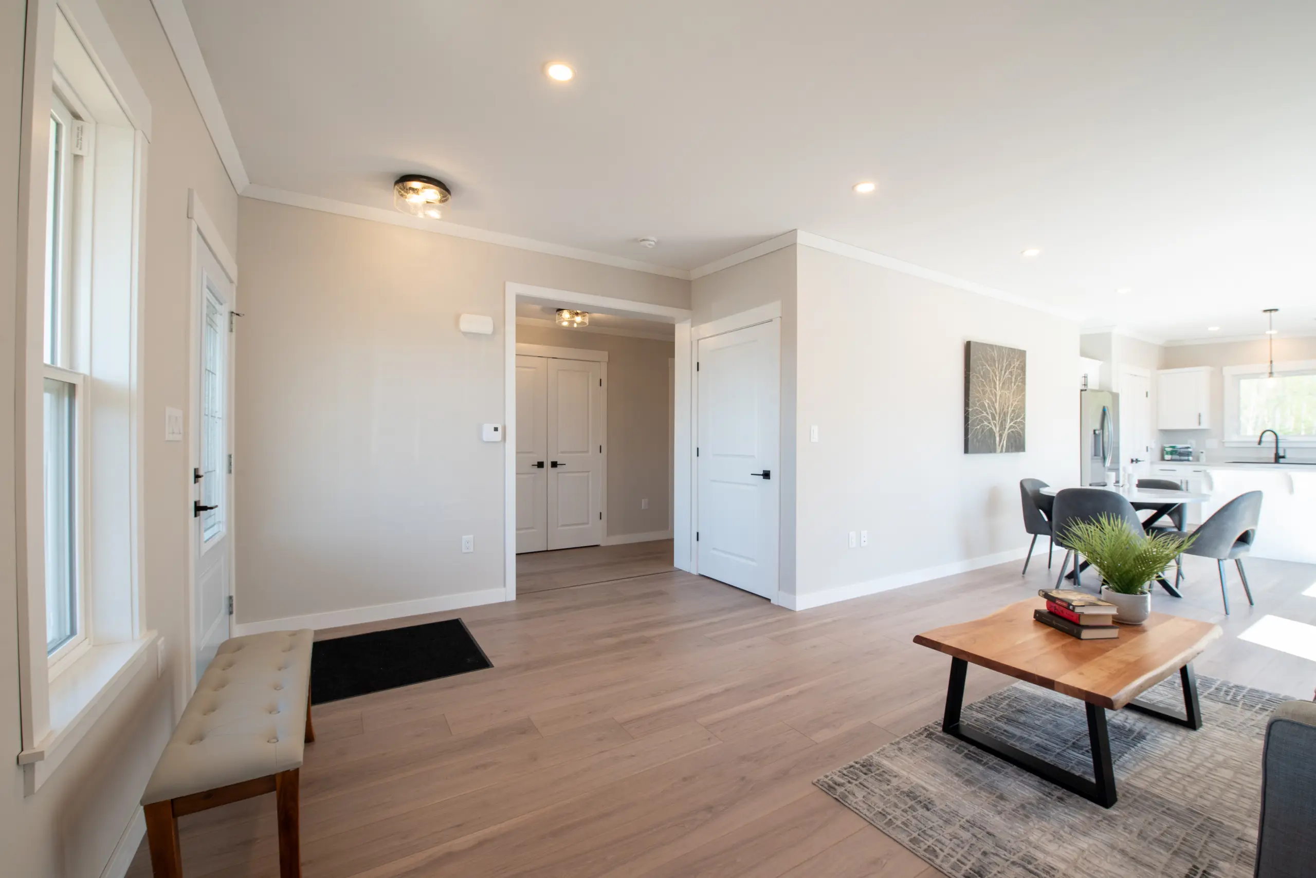 Bright open-concept living space with light wood flooring, neutral walls, a seating area, and views into the dining room and kitchen. 