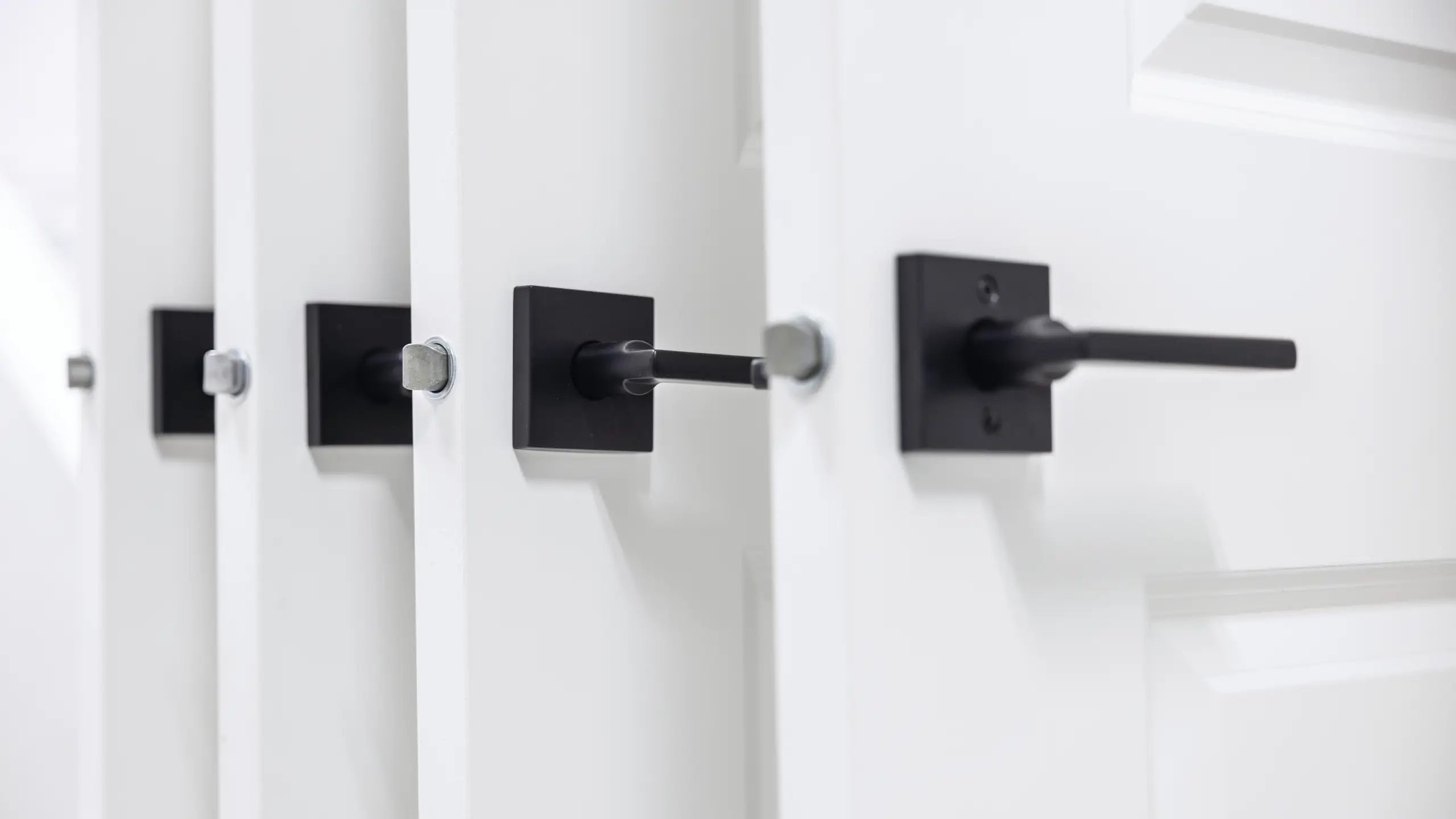 Close-up view of black rectangular door handles installed on white interior doors, aligned in a row. 