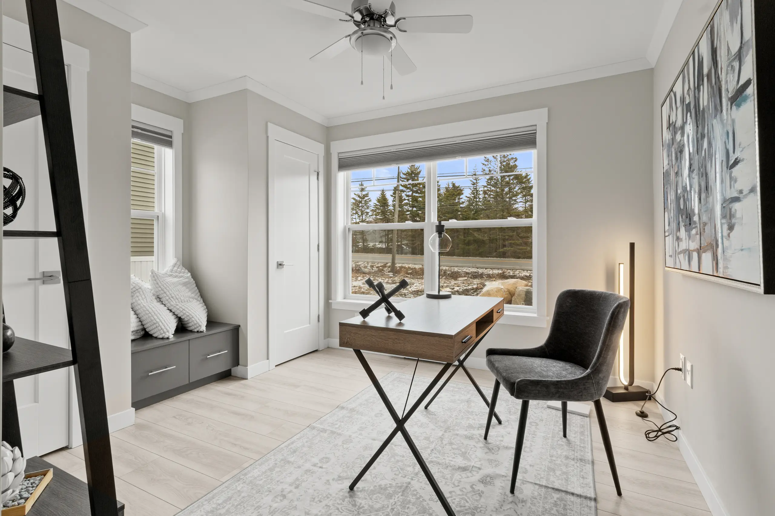 Modern home office featuring a wood desk, accent chair, large window, built-in storage, and contemporary décor. 