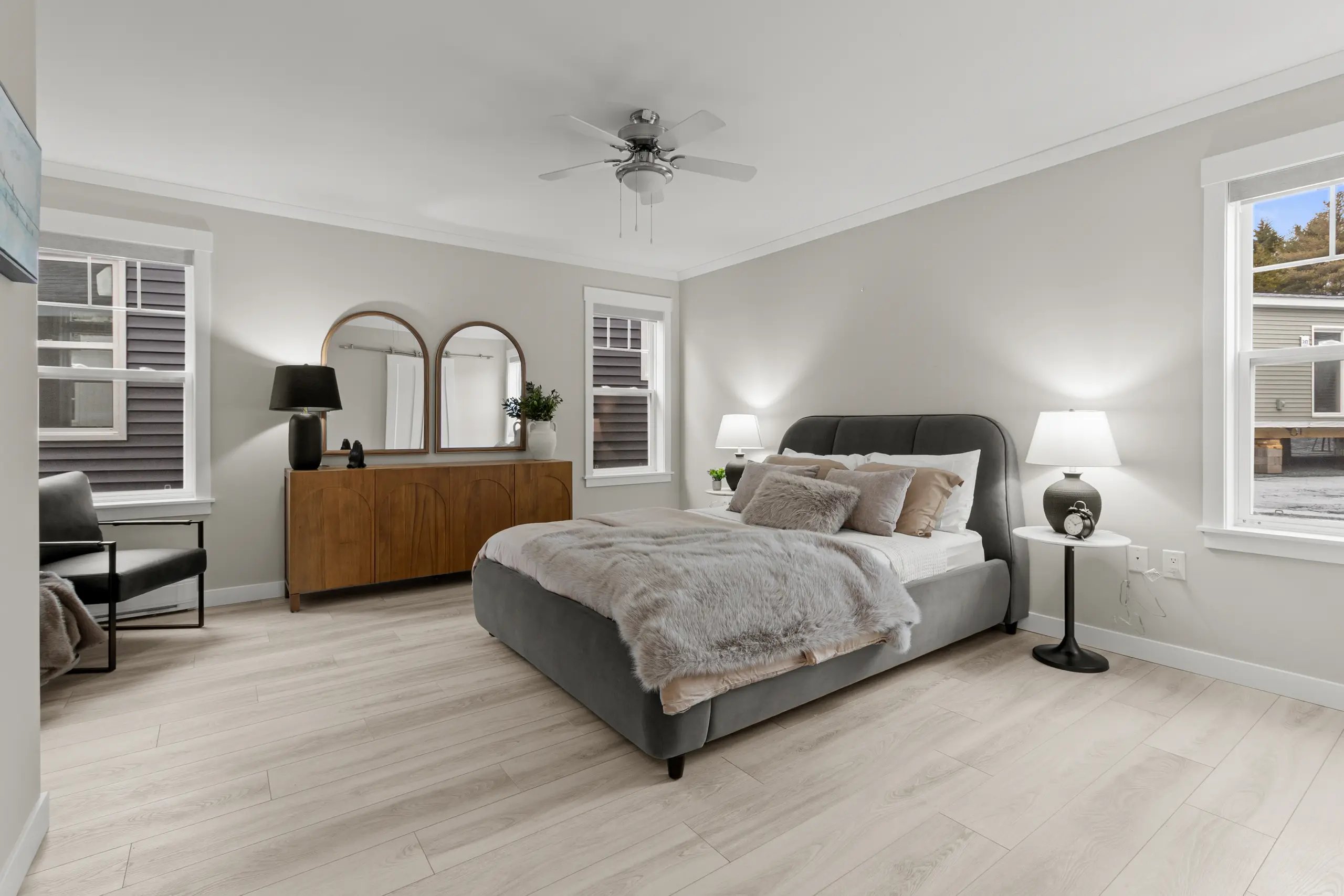 Spacious primary bedroom with an upholstered bed, modern furnishings, neutral tones, and abundant natural light. 