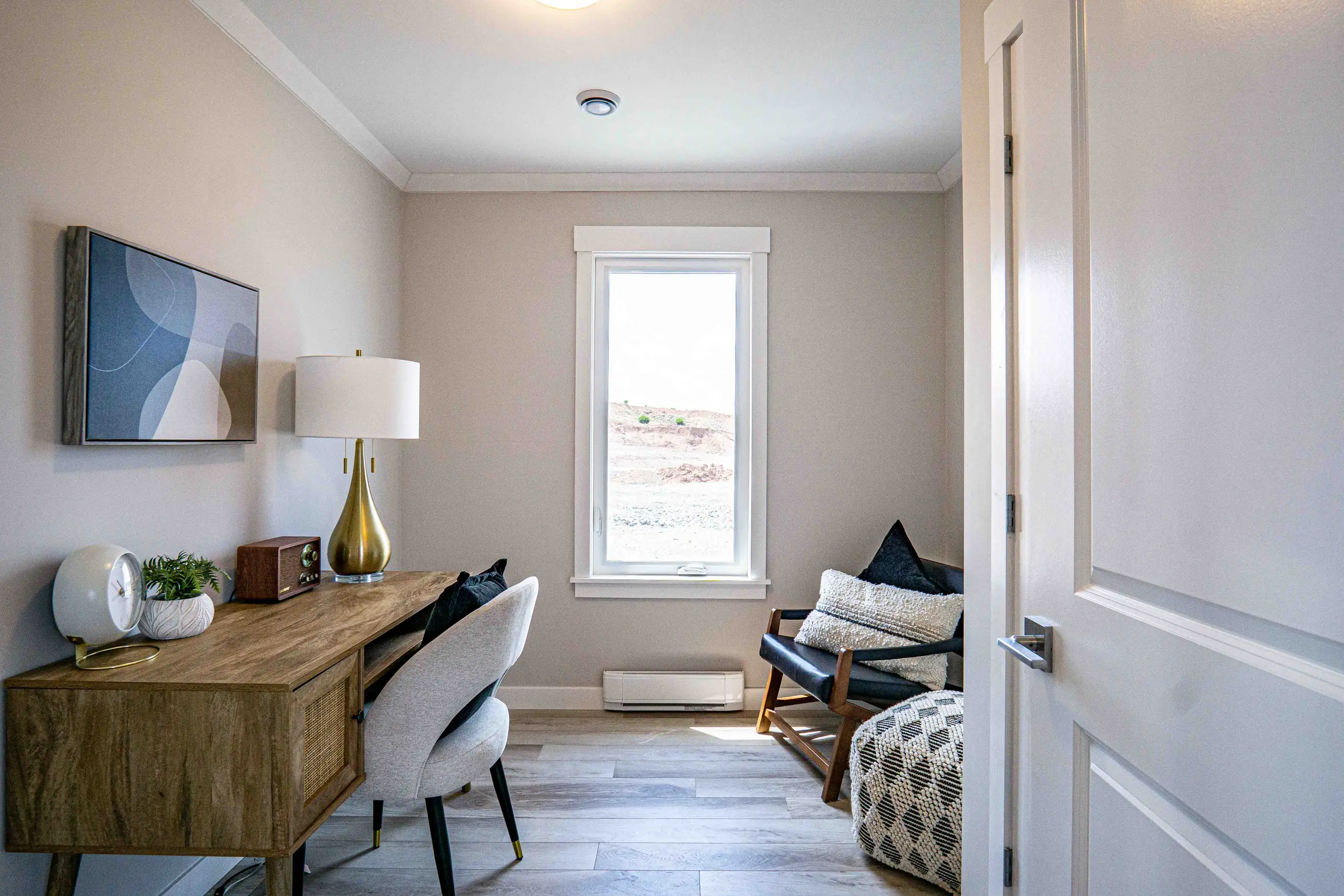 Multi-purpose room styled as a home office with a desk, seating area, and large window providing natural light. 