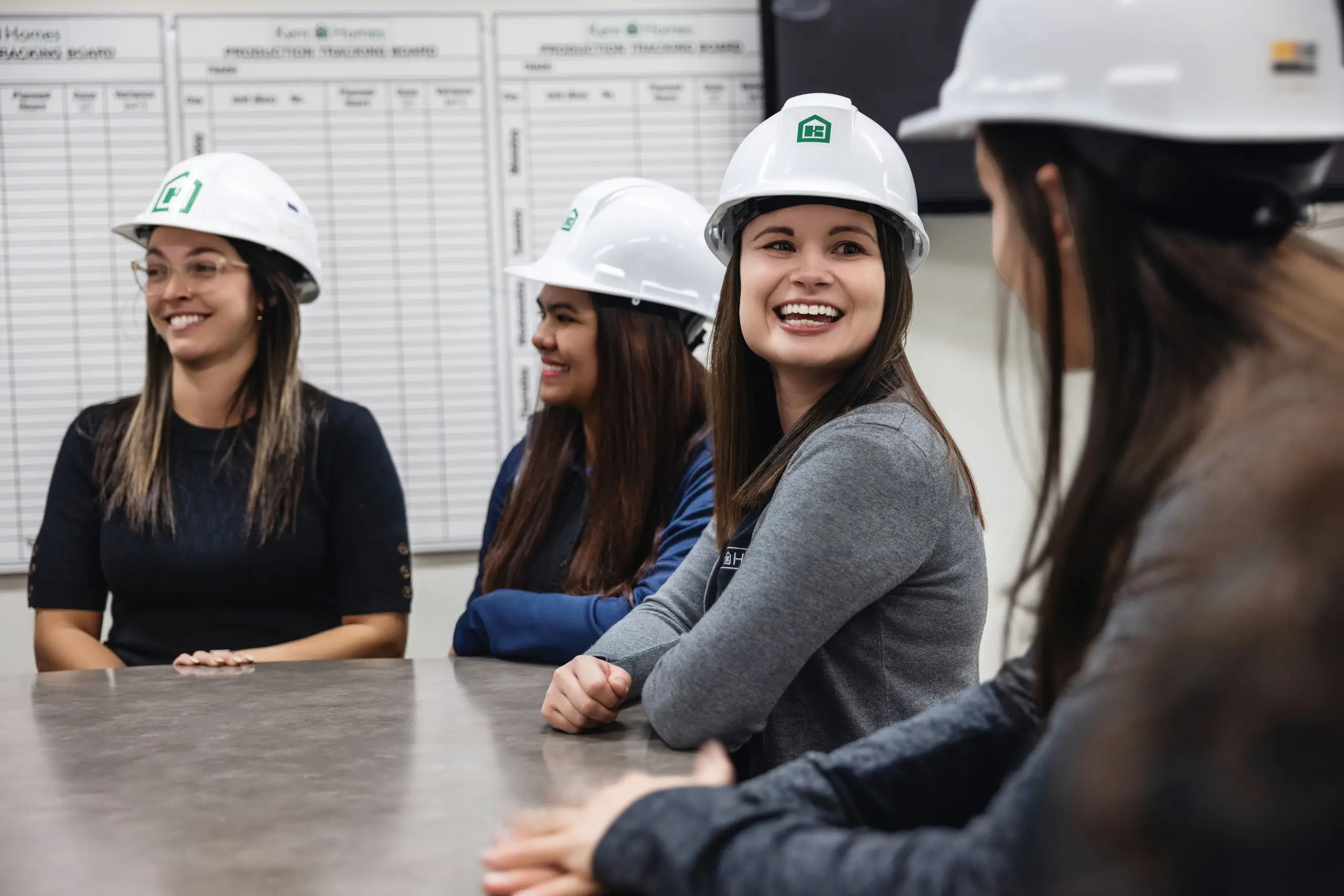 Kent Homes team members wearing hard hats gathered around a table, participating in a discussion inside the manufacturing facility. 