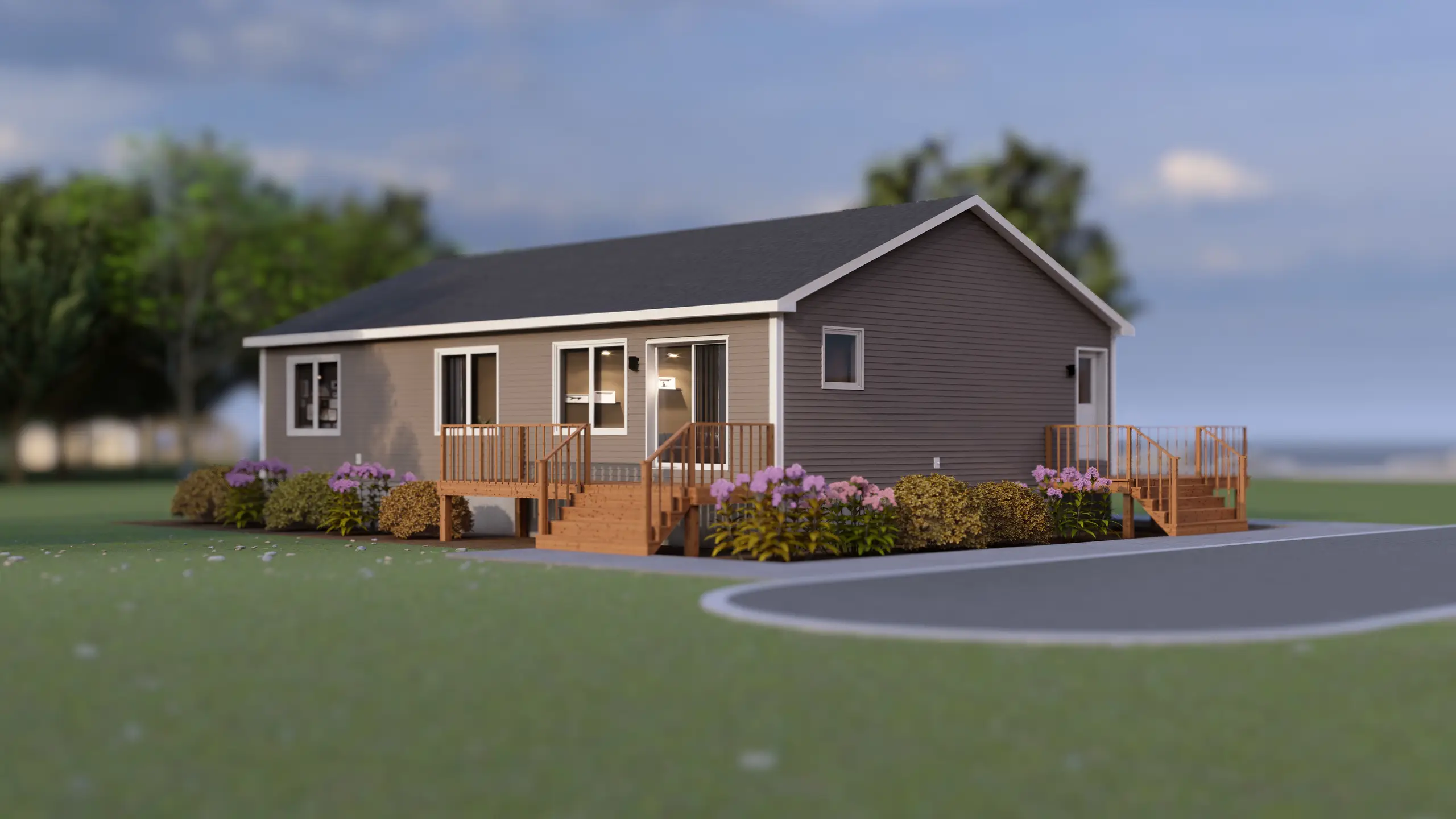 Angled front view of a single-storey modular home with grey siding, white trim, a gable roof, twin wooden entry decks with stairs, and landscaped shrubs and flowers along the foundation. 