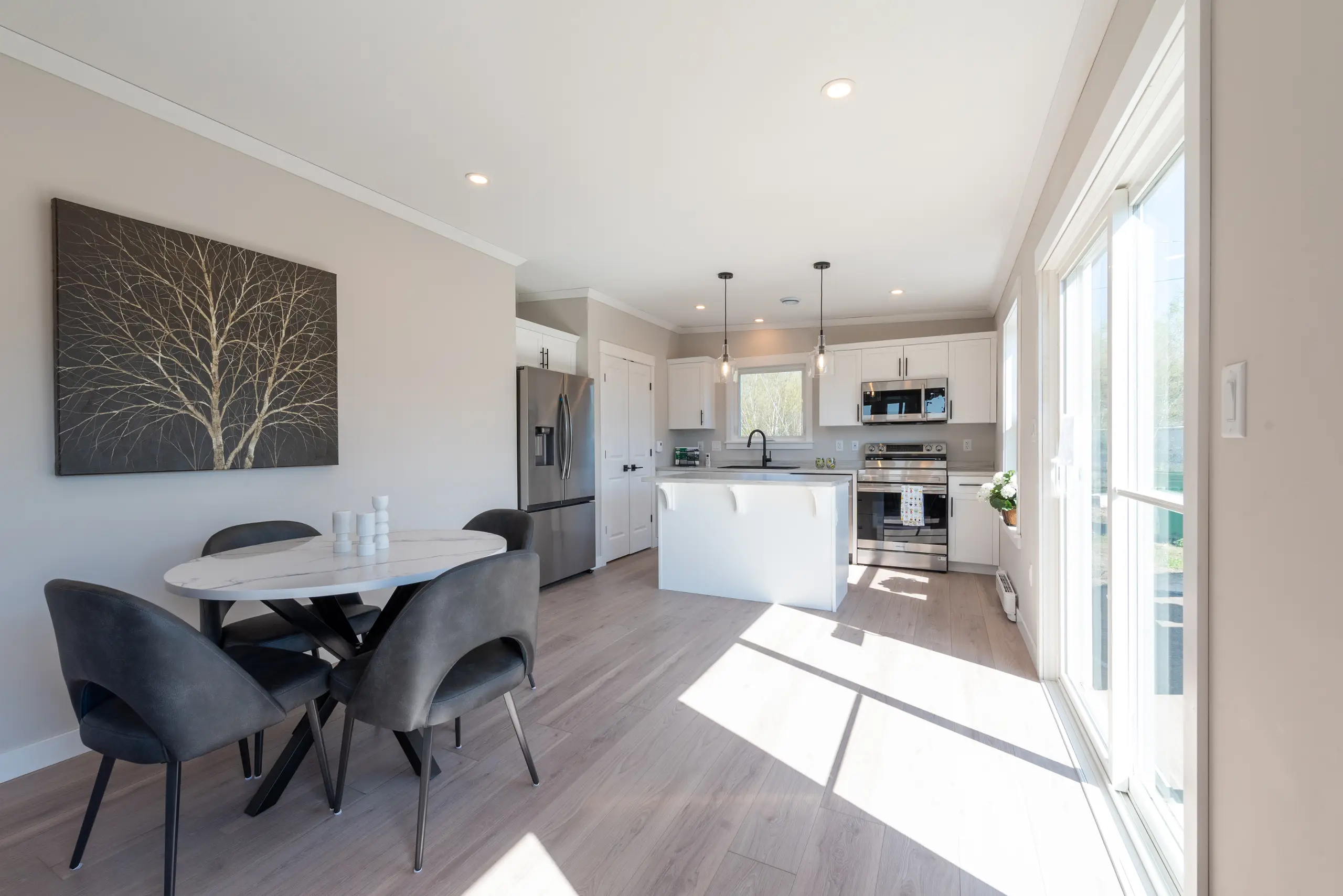 Bright open-concept living space with light wood flooring, neutral walls, a seating area, and views into the dining room and kitchen. 