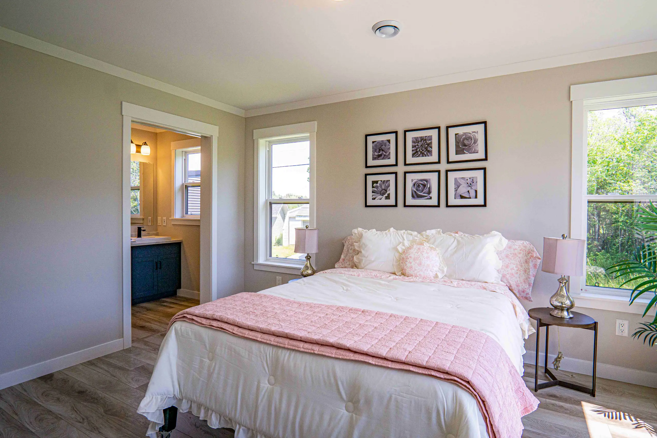 Spacious primary bedroom with a large bed, soft neutral finishes, abundant natural light, and an ensuite bathroom entrance. 