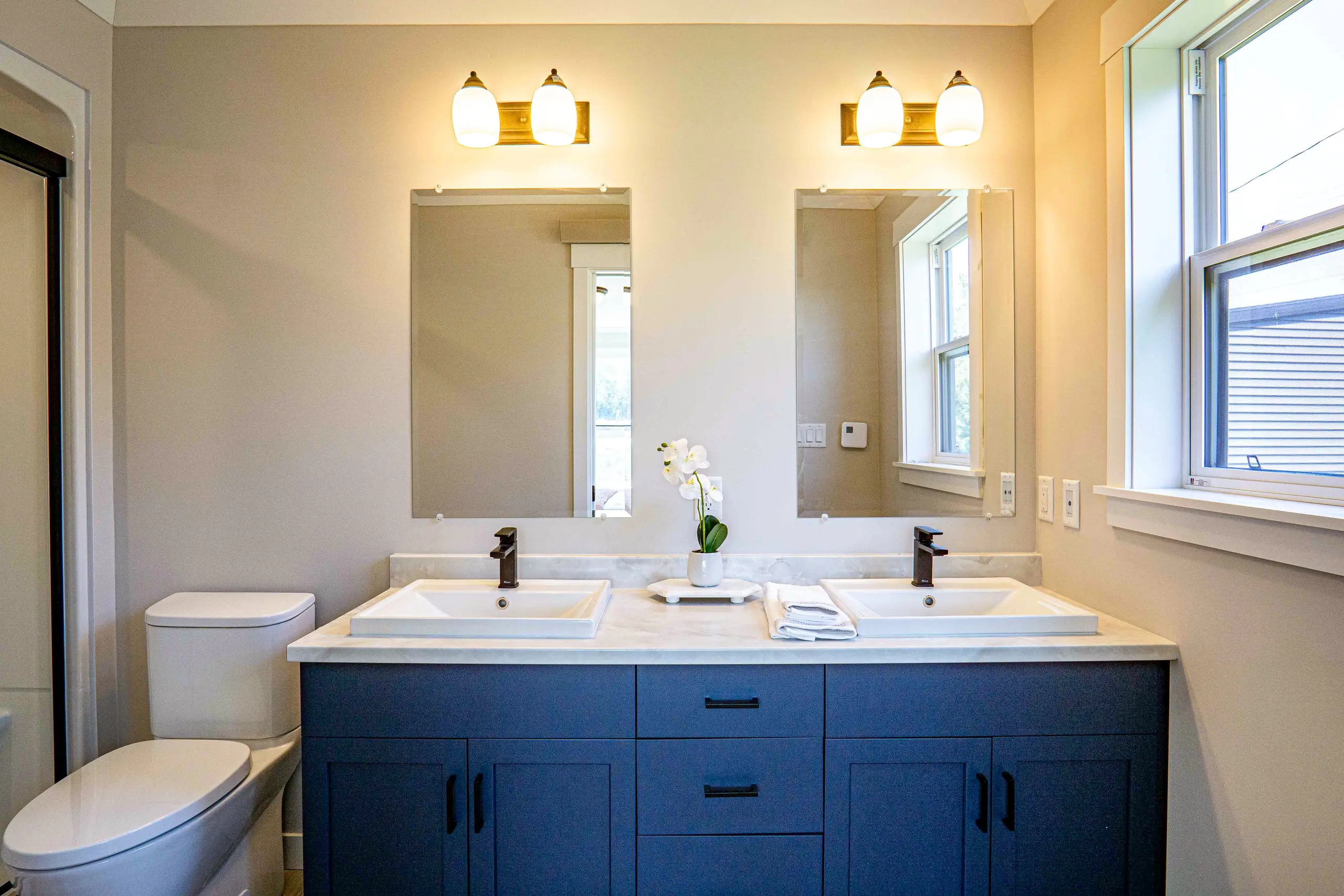 Contemporary ensuite bathroom with a double-sink vanity, sleek dark cabinetry, large mirrors, and bright natural light. 