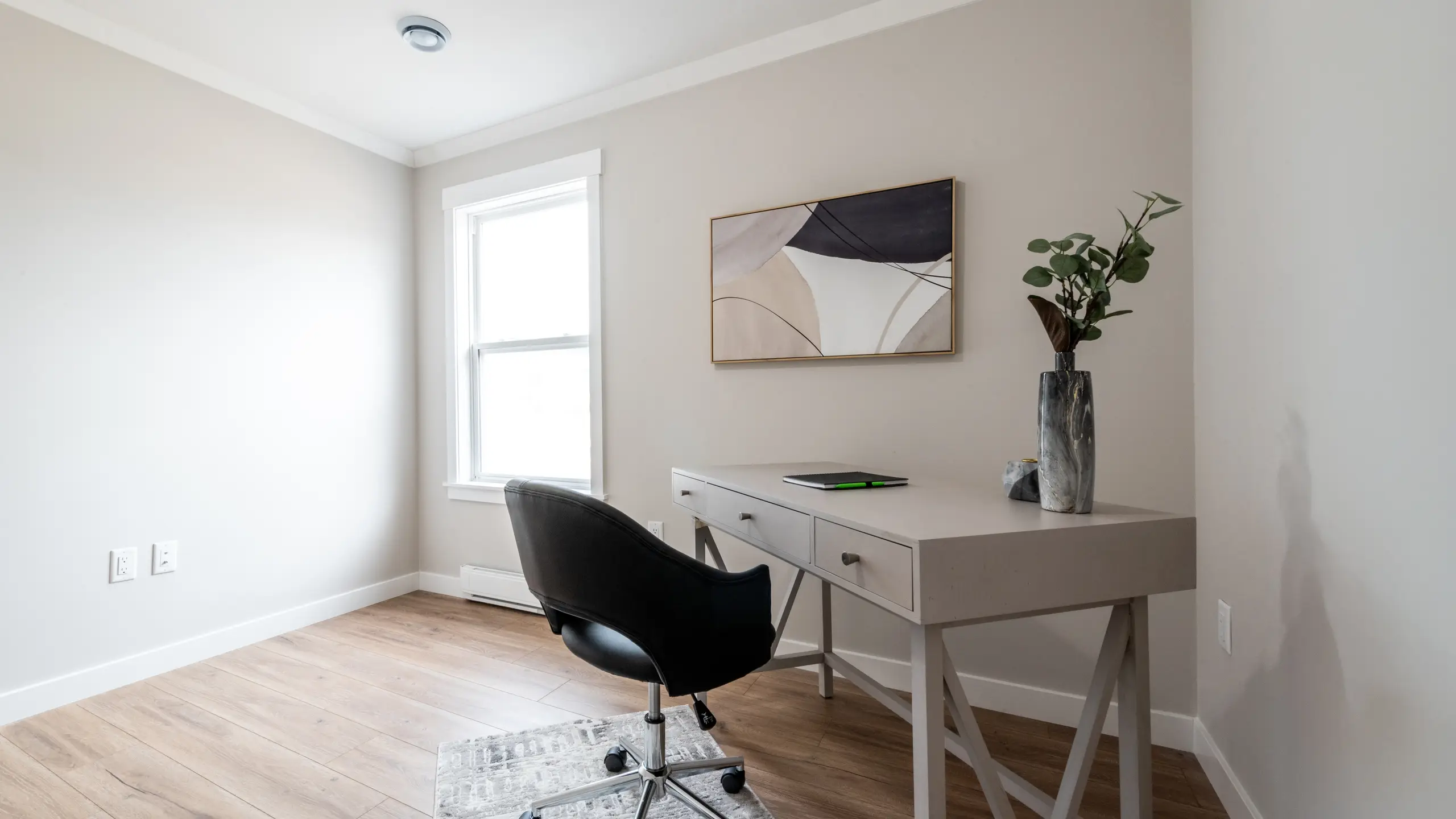 Home office with a modern desk, chair, decorative artwork, and a window providing natural light. 