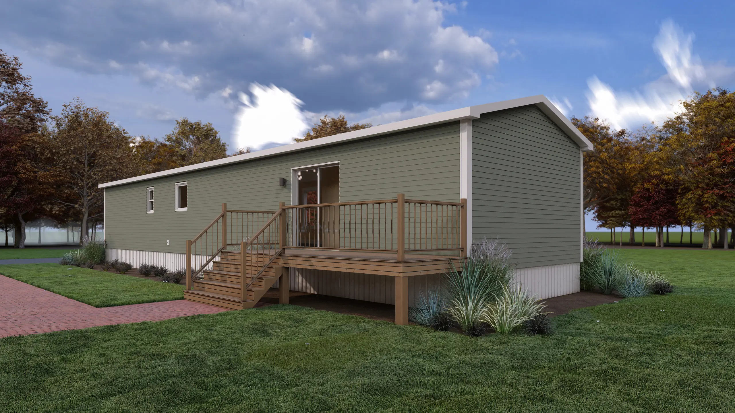 Rear angled view of a modern mini home featuring a spacious raised wood deck, sliding patio door, sage green siding, and ornamental grass landscaping. 