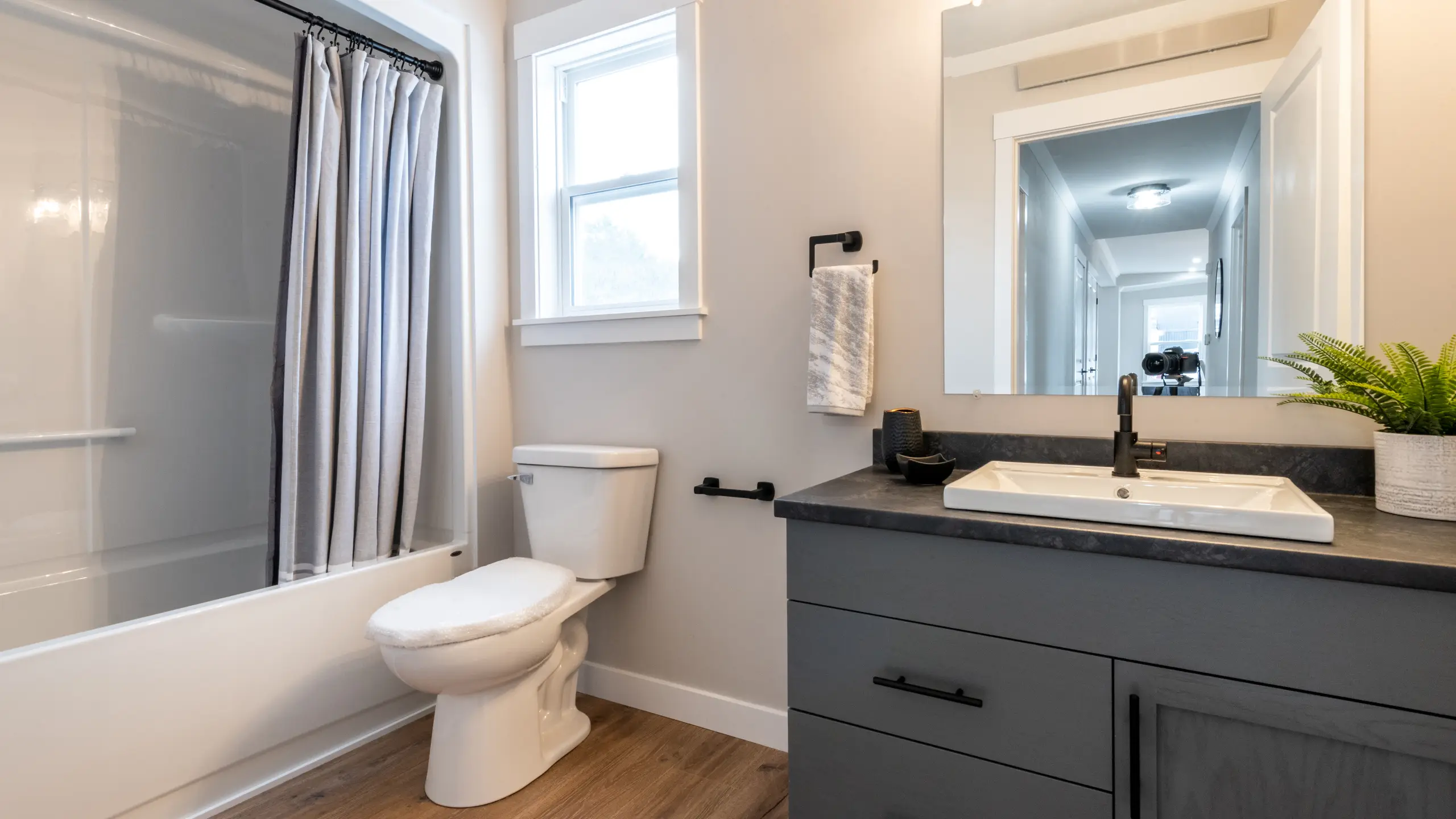 Bathroom with a tub and shower curtain, toilet, and grey vanity with sink and mirror under bright lighting. 