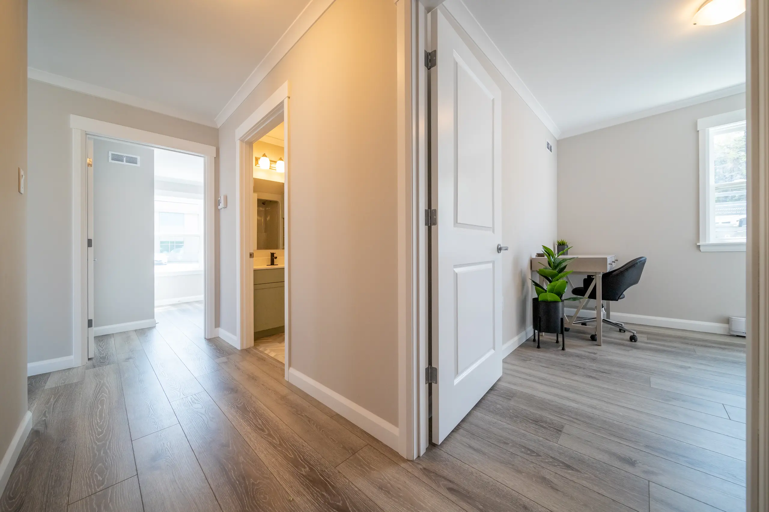 Hallway with wood-look flooring leading to a home office or flex room furnished with a desk and chair. 
