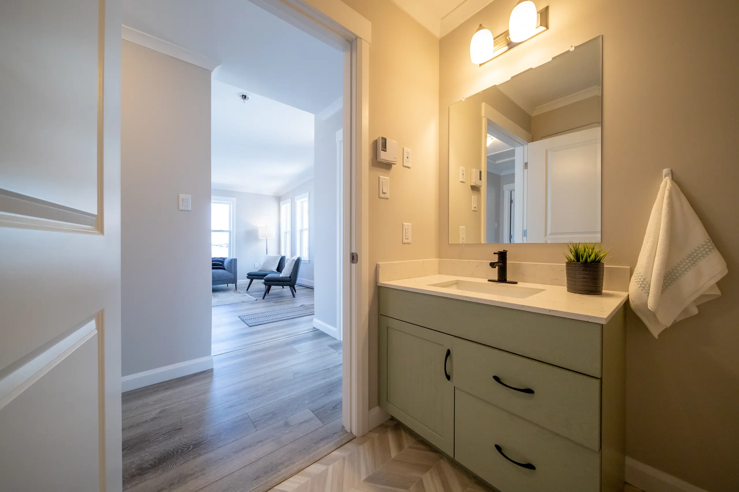 Modern bathroom with a sage green vanity, quartz countertop, black fixtures, and bright overhead lighting. 