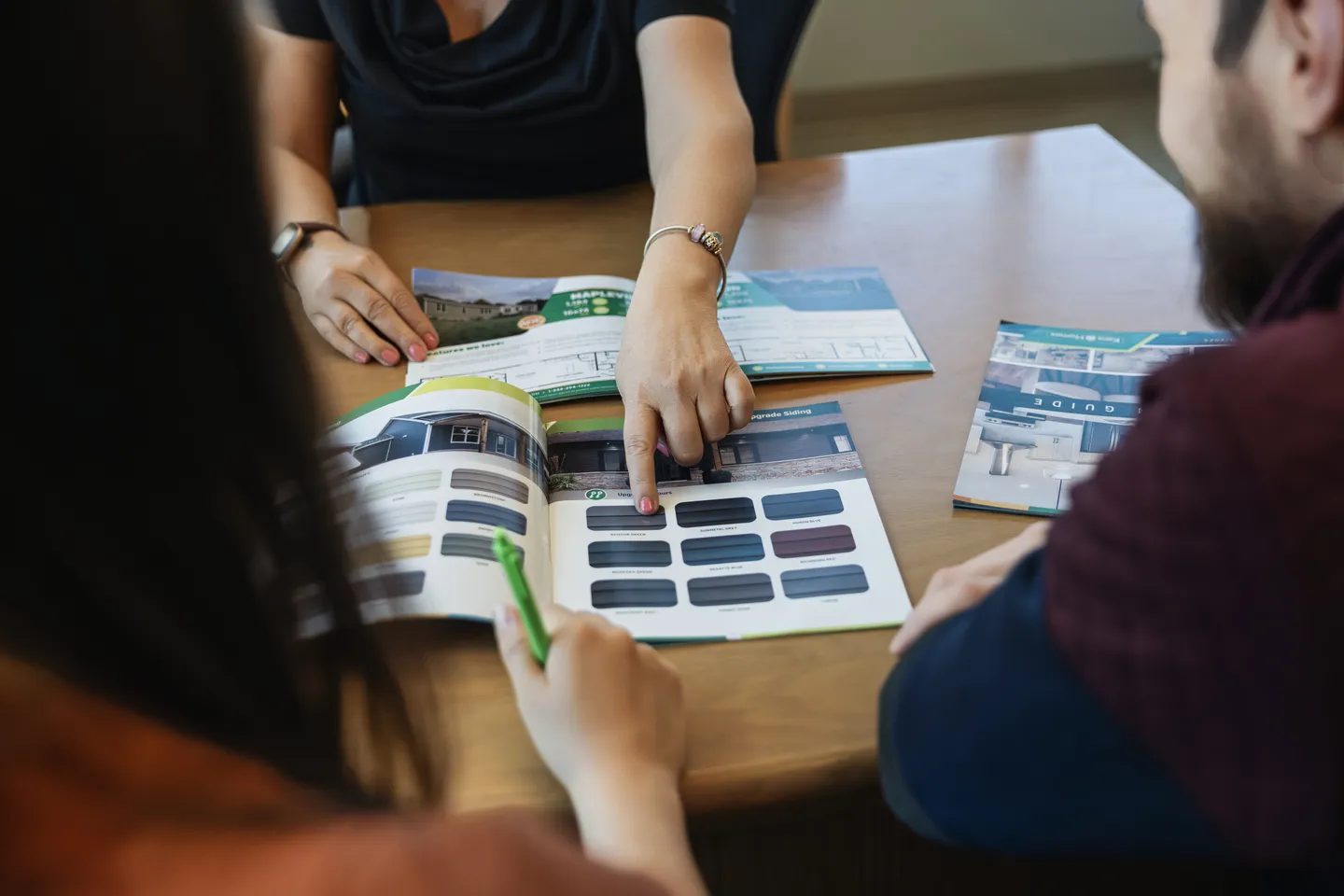 Three individuals seated at a table reviewing Kent Homes marketing brochures, with one person pointing to exterior colour and design options while others look on and take notes 