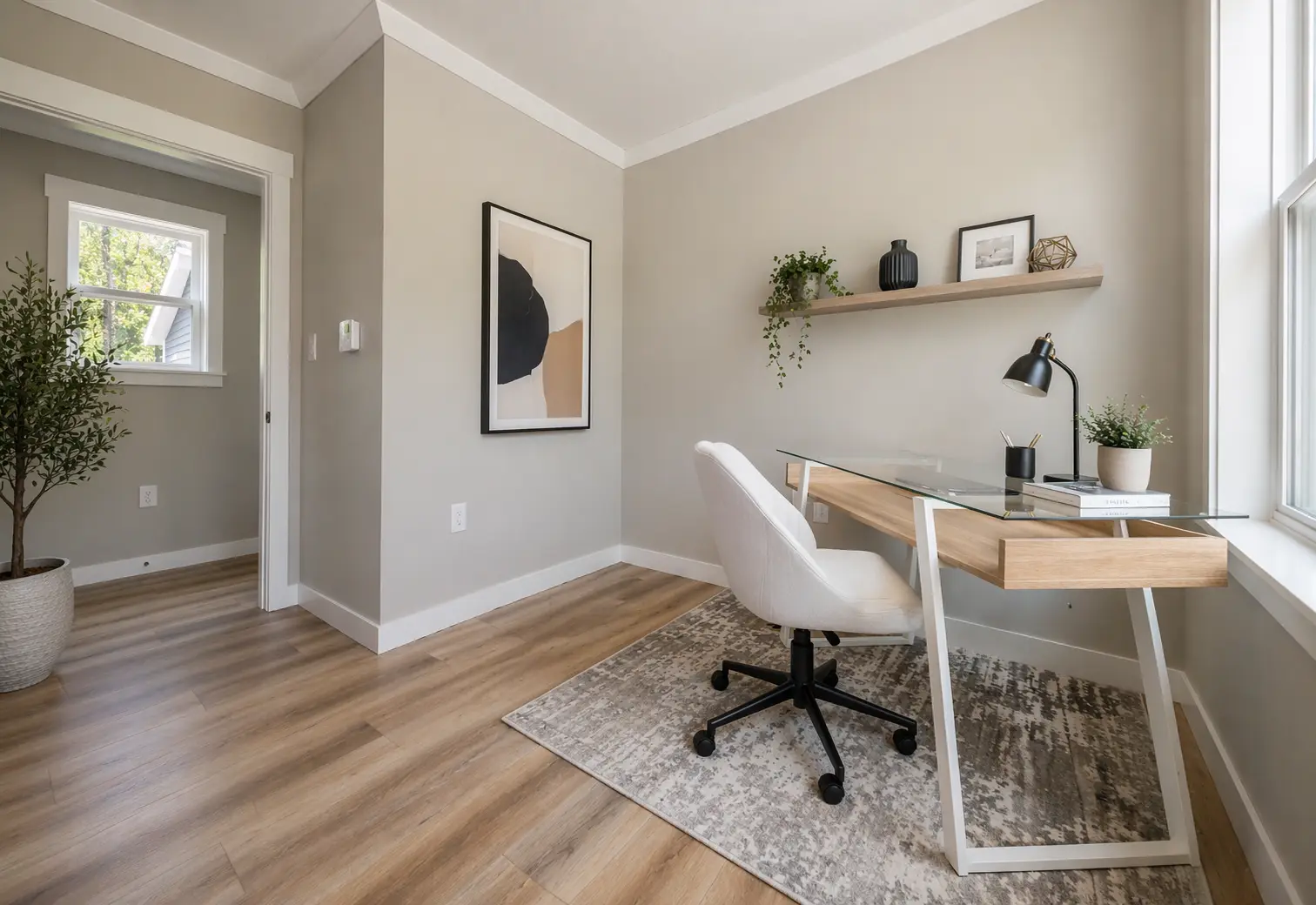 Functional home office with a glass-top desk, upholstered task chair, floating shelf, and large window providing natural light. 