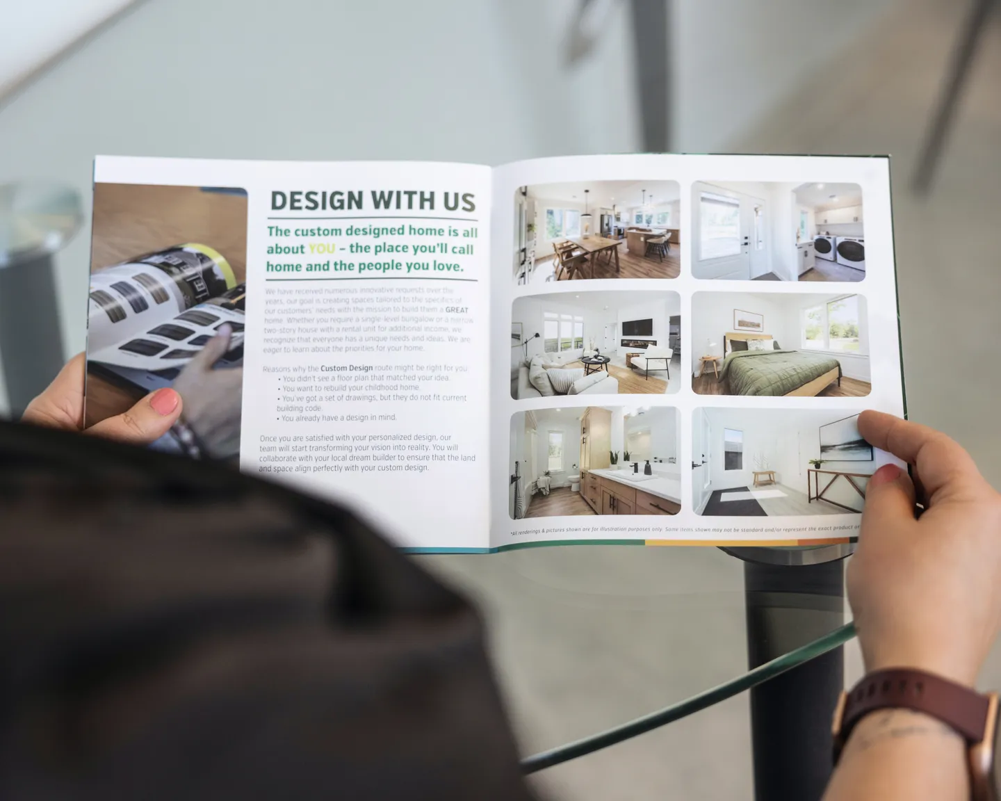 Person holding an open Kent Homes design guide showing custom home inspiration, including interior photos and design options, while seated at a table 