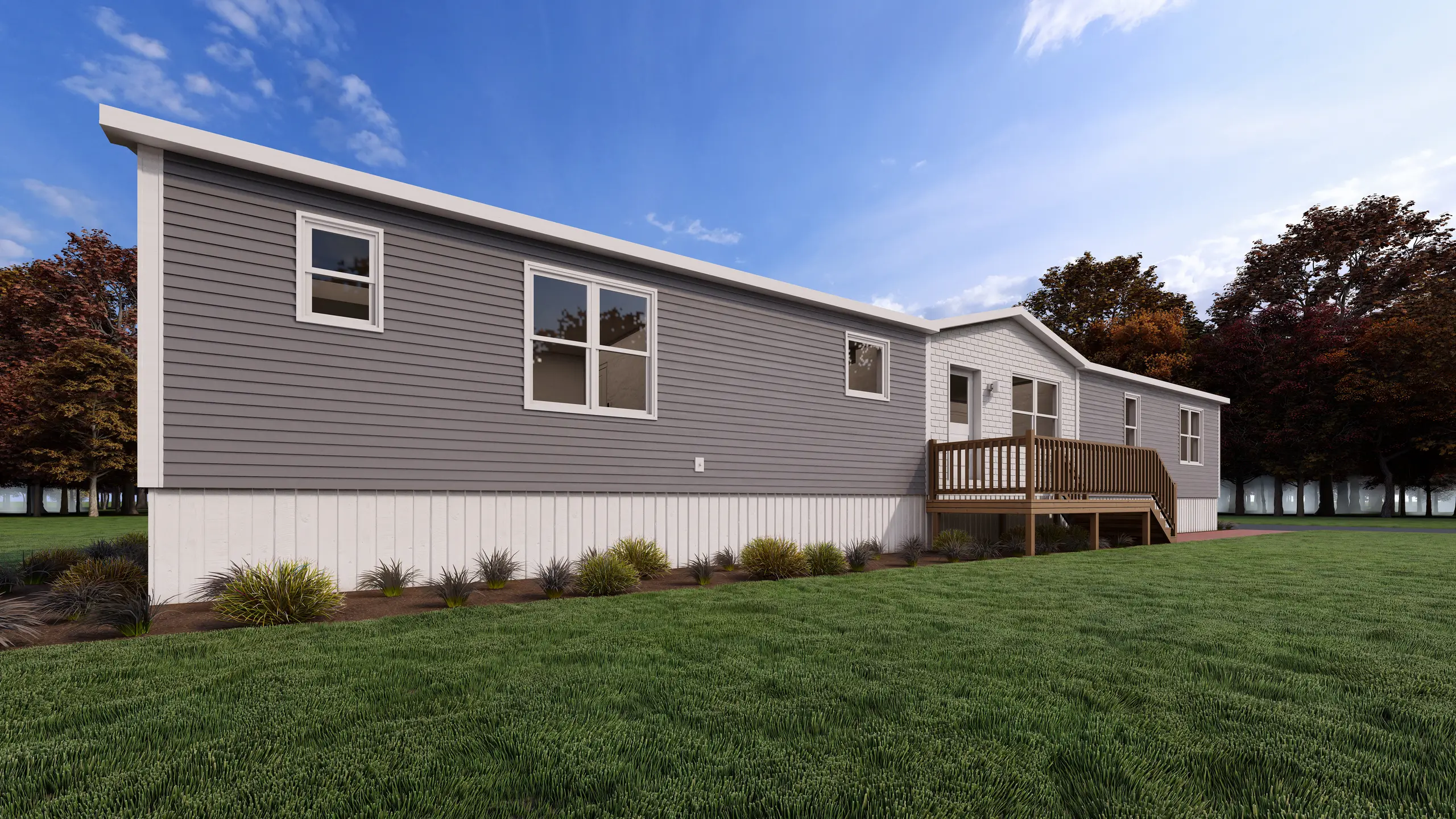 Front corner view of a contemporary mini home showcasing grey siding, a white shingle accent entry, wood deck, and landscaped foundation beds. 