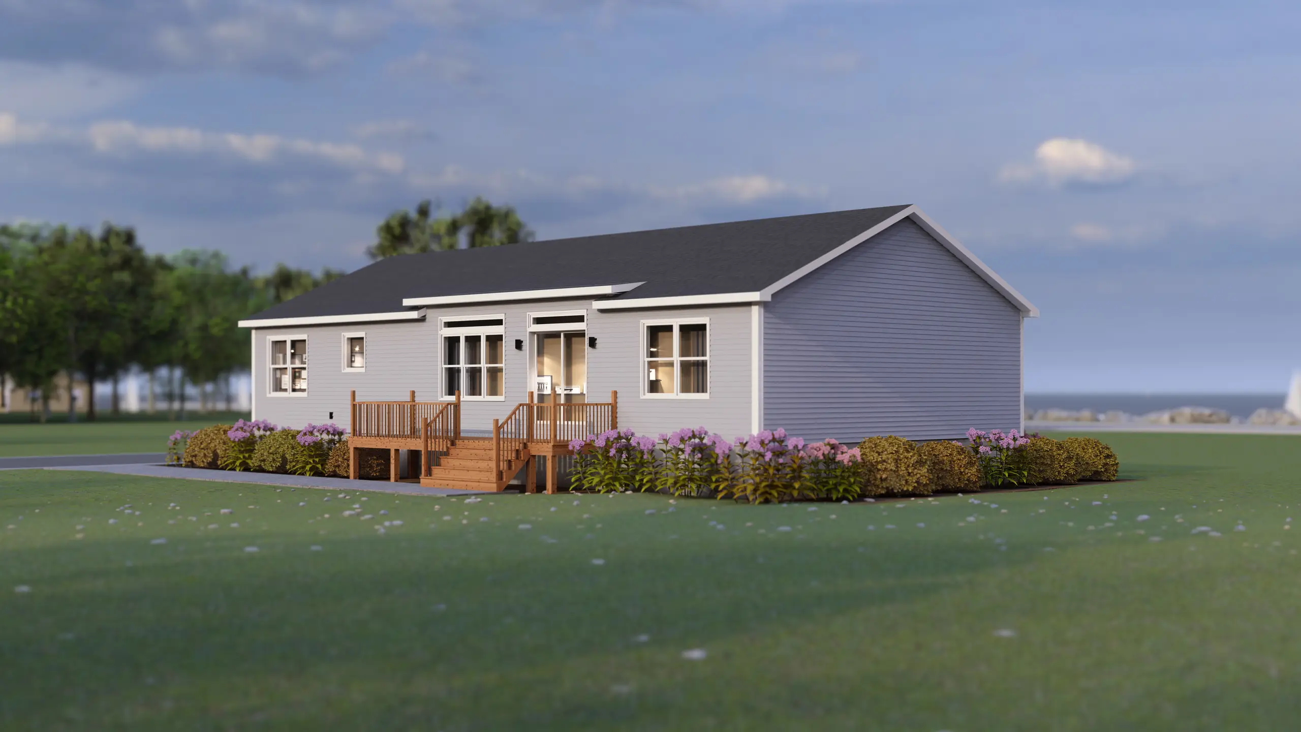 Rear view of a contemporary modular bungalow featuring a central deck, large patio doors, light grey siding, and landscaped flower beds. 