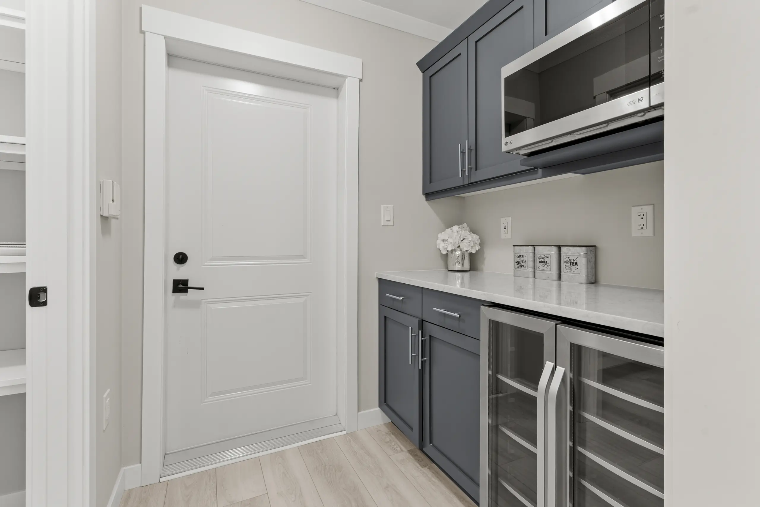 Built-in beverage station with glass-front beverage coolers, microwave, cabinetry, and countertop storage space. 