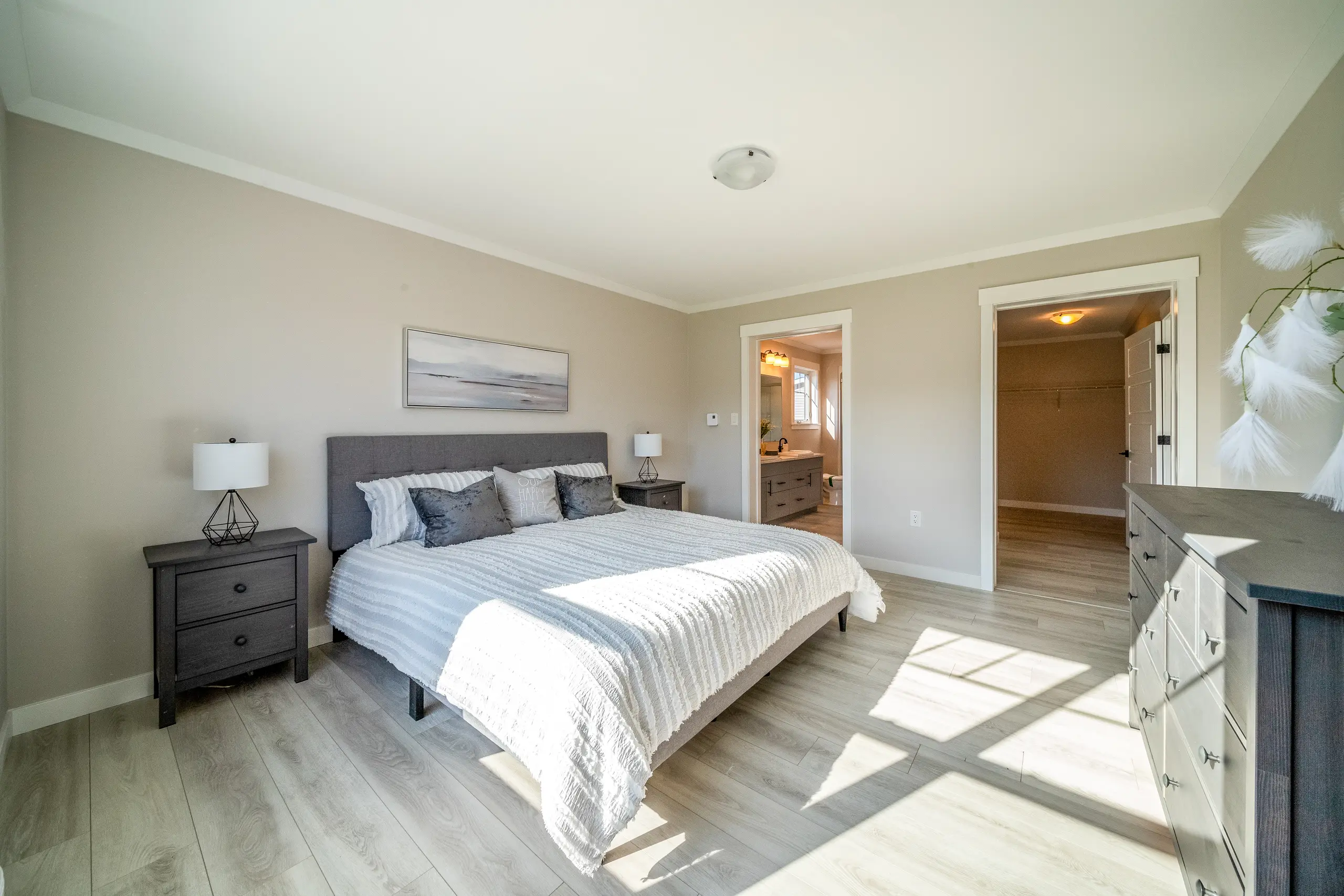 Spacious primary bedroom featuring a neutral color palette, large bed, walk-in closet access, and ensuite bathroom entry. 