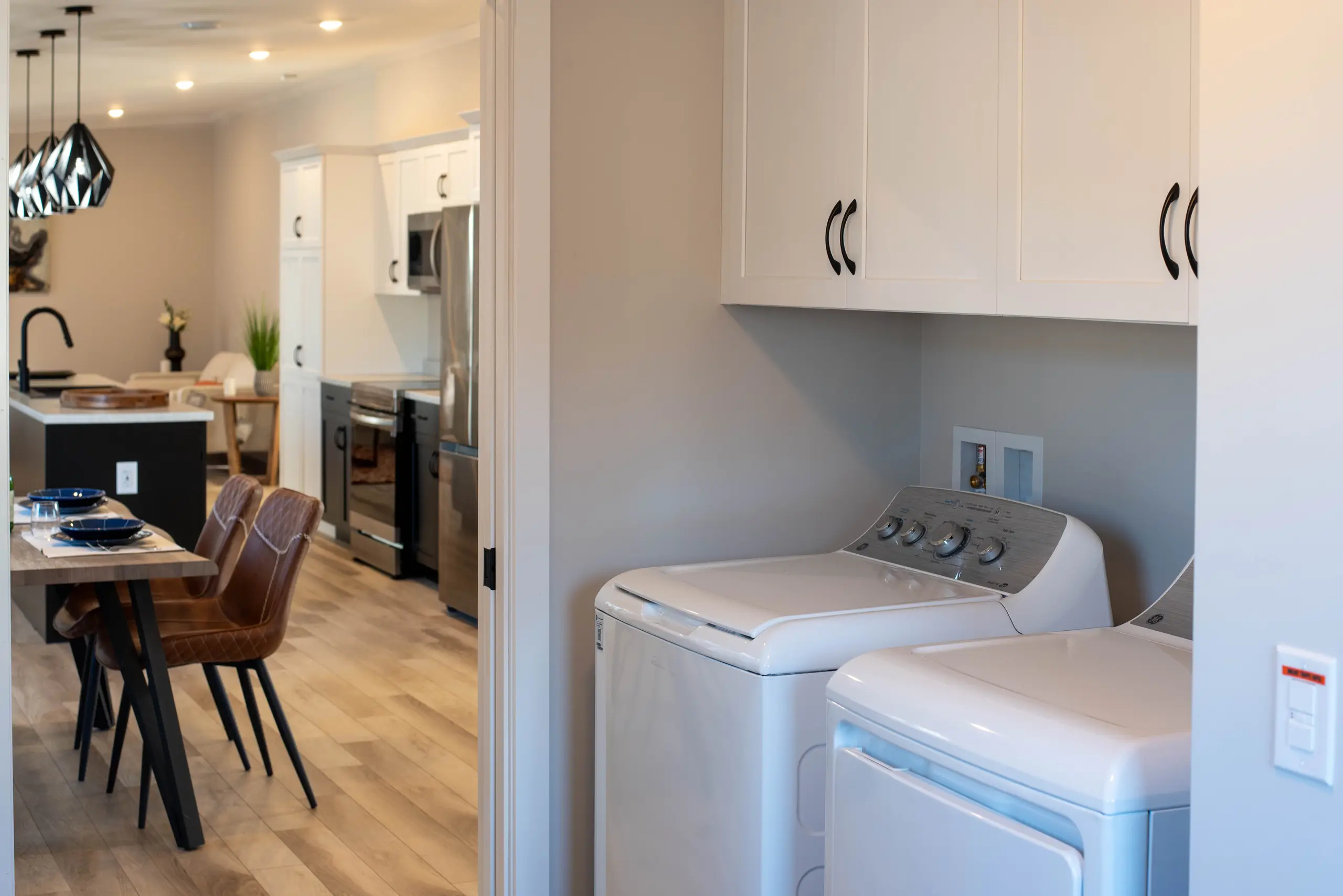 Convenient laundry area with a washer and dryer, overhead storage cabinets, and easy access to the kitchen and dining space. 