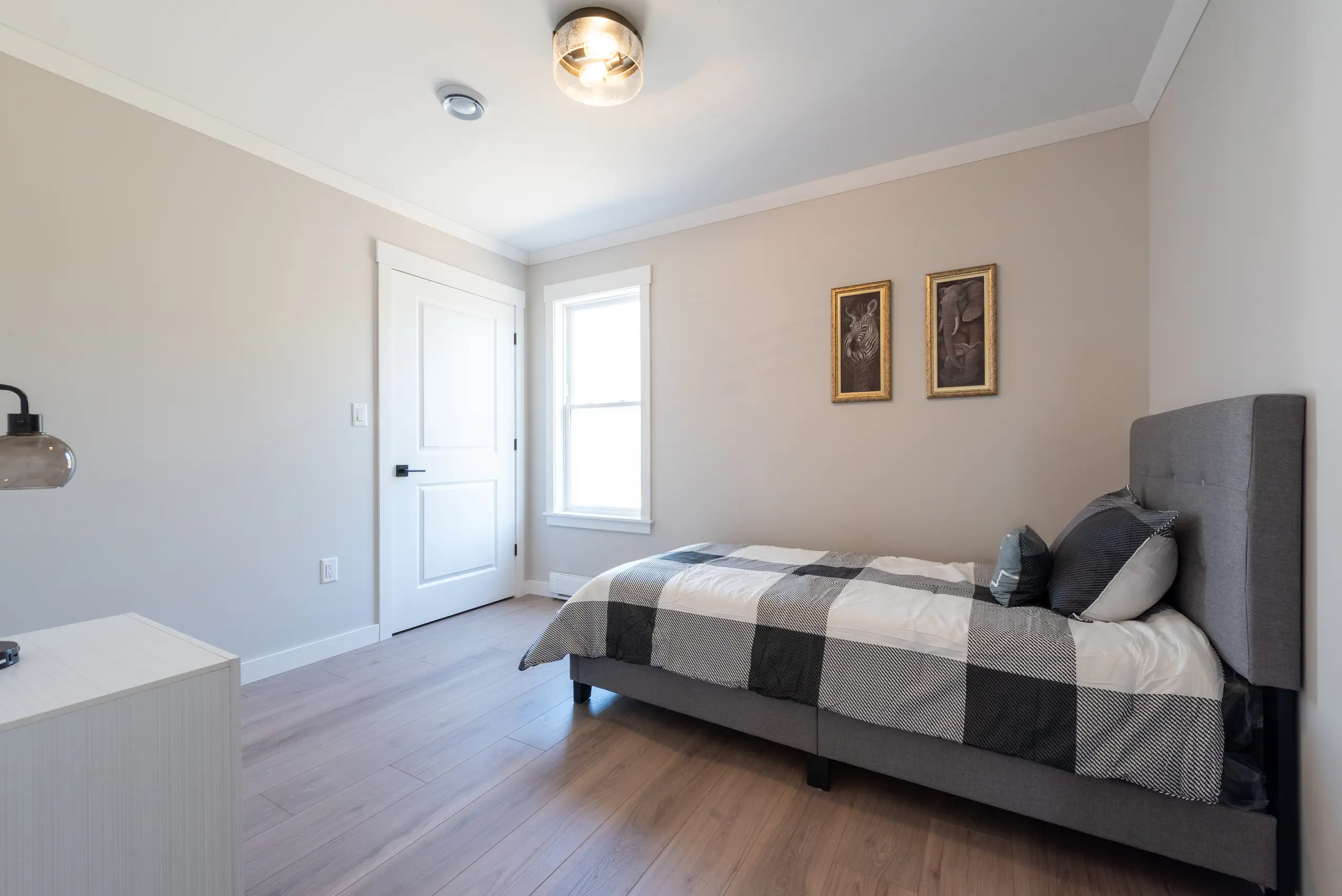 Cozy bedroom with a grey upholstered bed, neutral décor, a large window, and light wood flooring. 