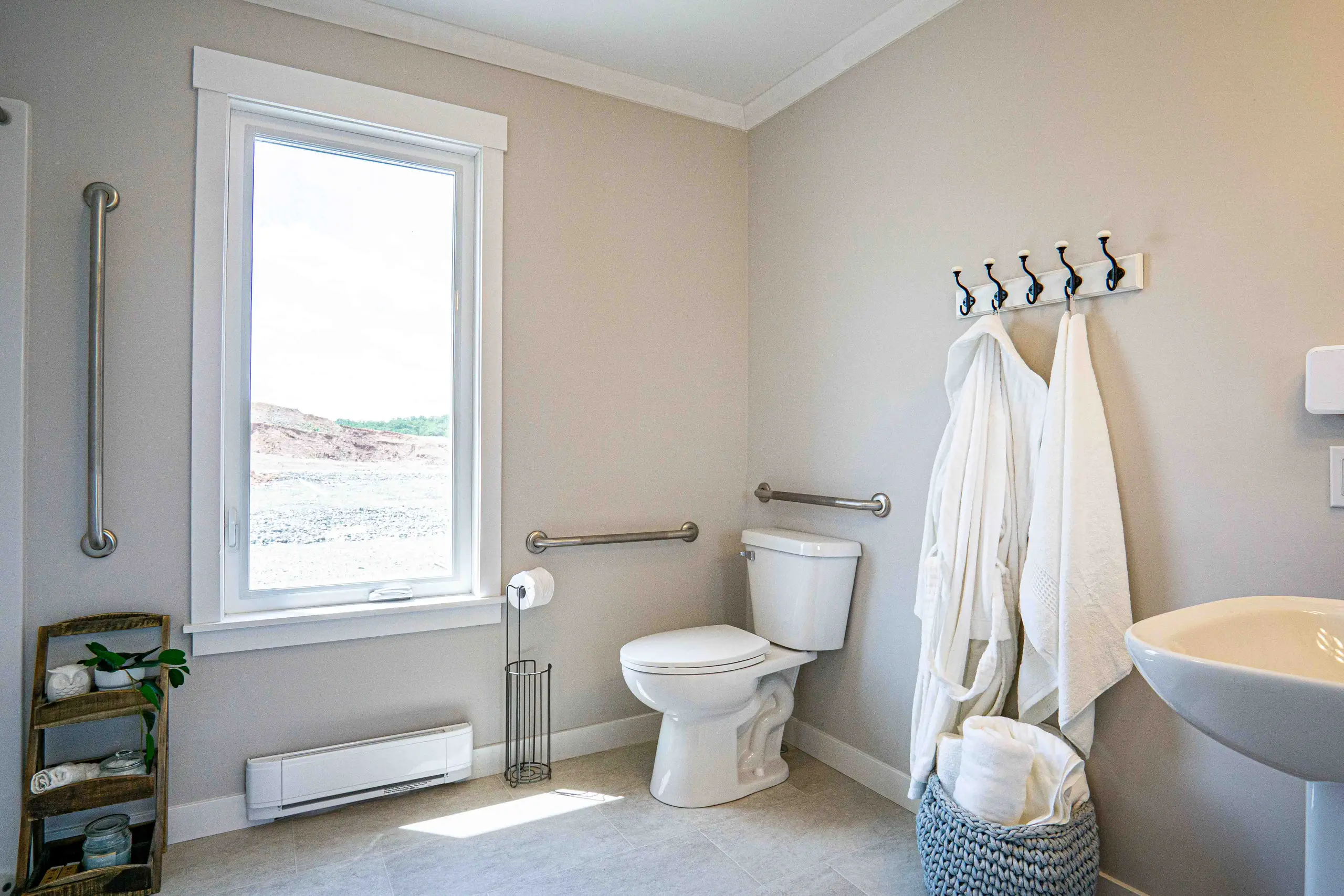 Barrier-free bathroom featuring grab bars, wide clearances, accessible fixtures, and a large window for natural light. 