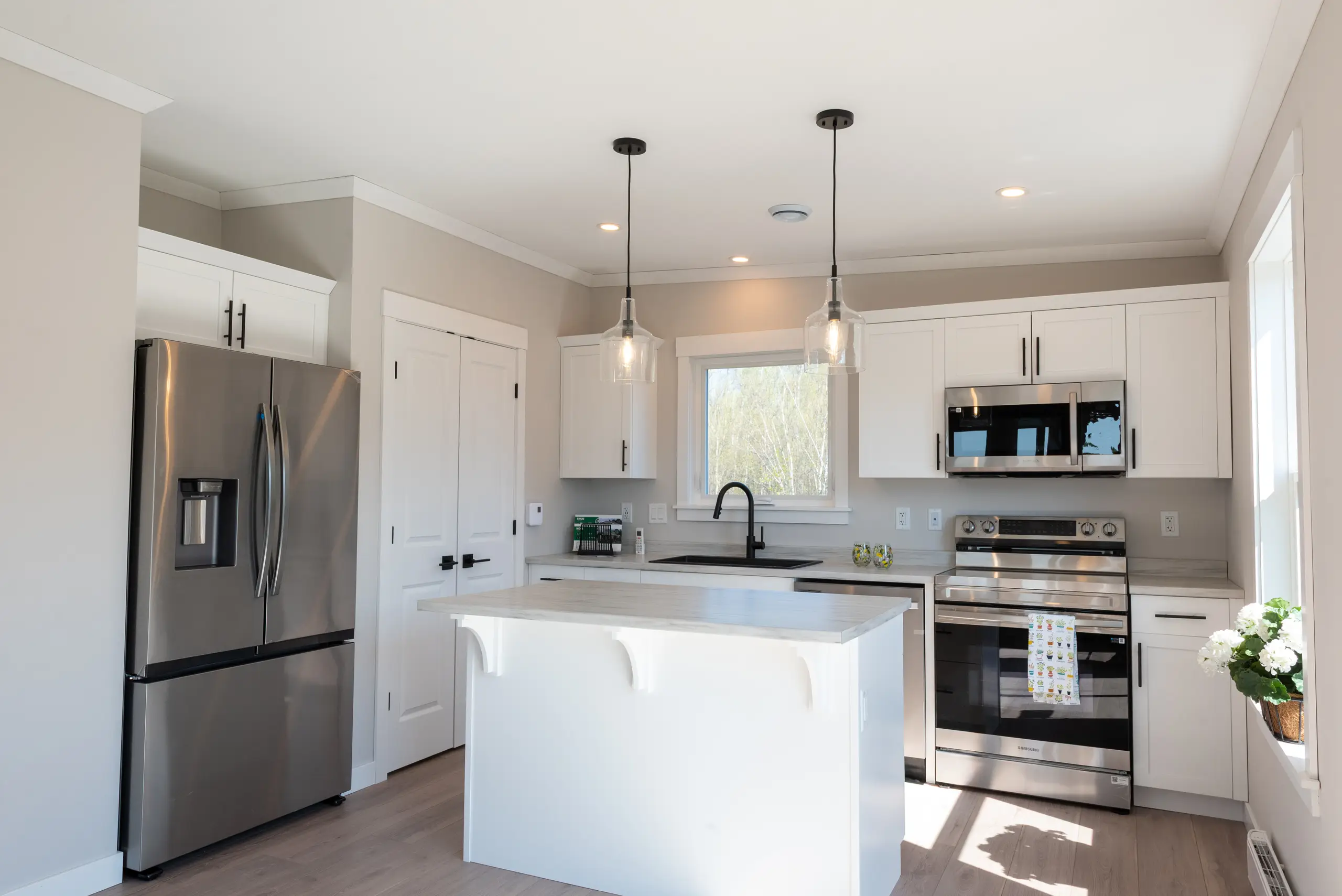 Contemporary kitchen with white shaker cabinets, stainless steel appliances, pendant lighting, and a central island with seating space. 