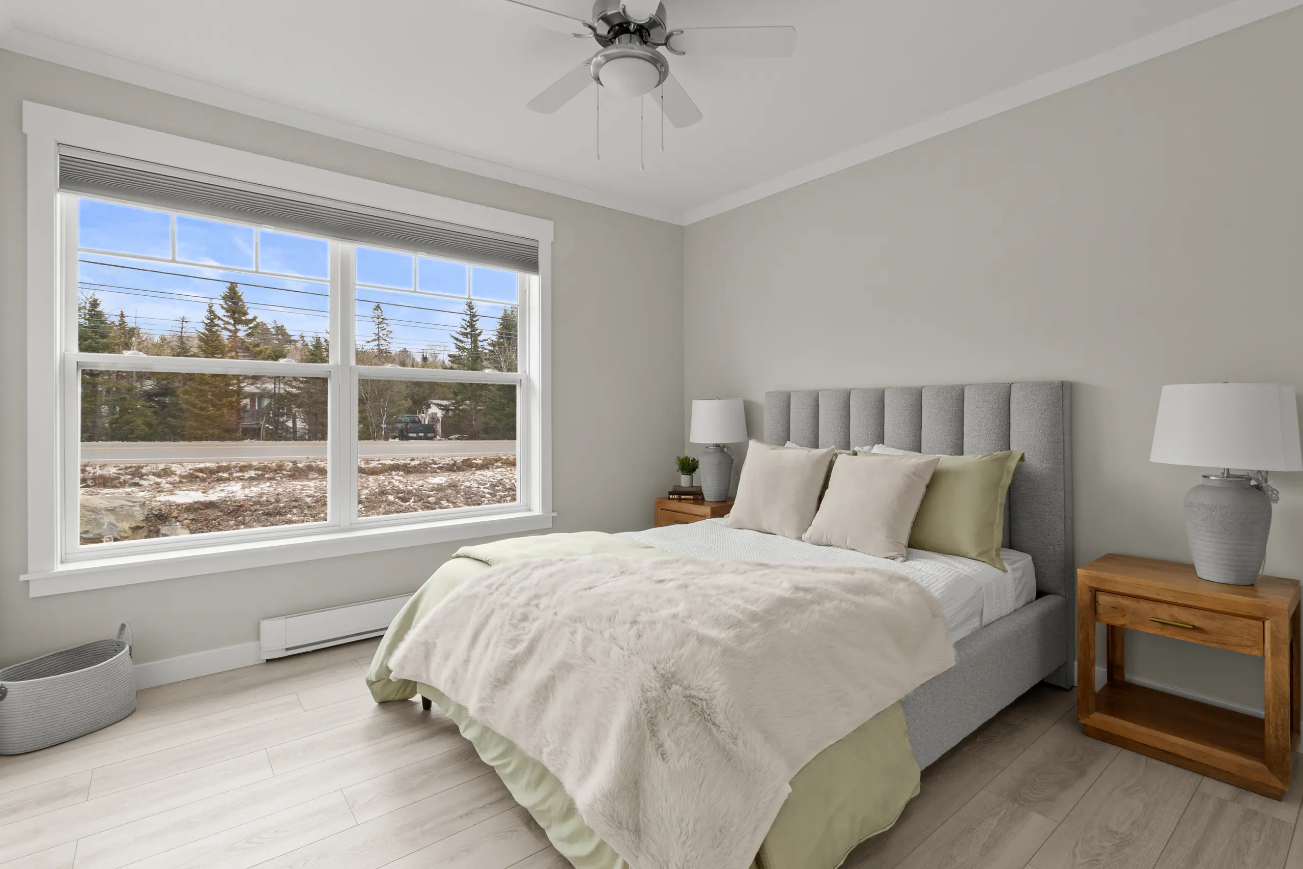 Cozy bedroom with a large window, upholstered bed, soft neutral bedding, and natural wood nightstands. 