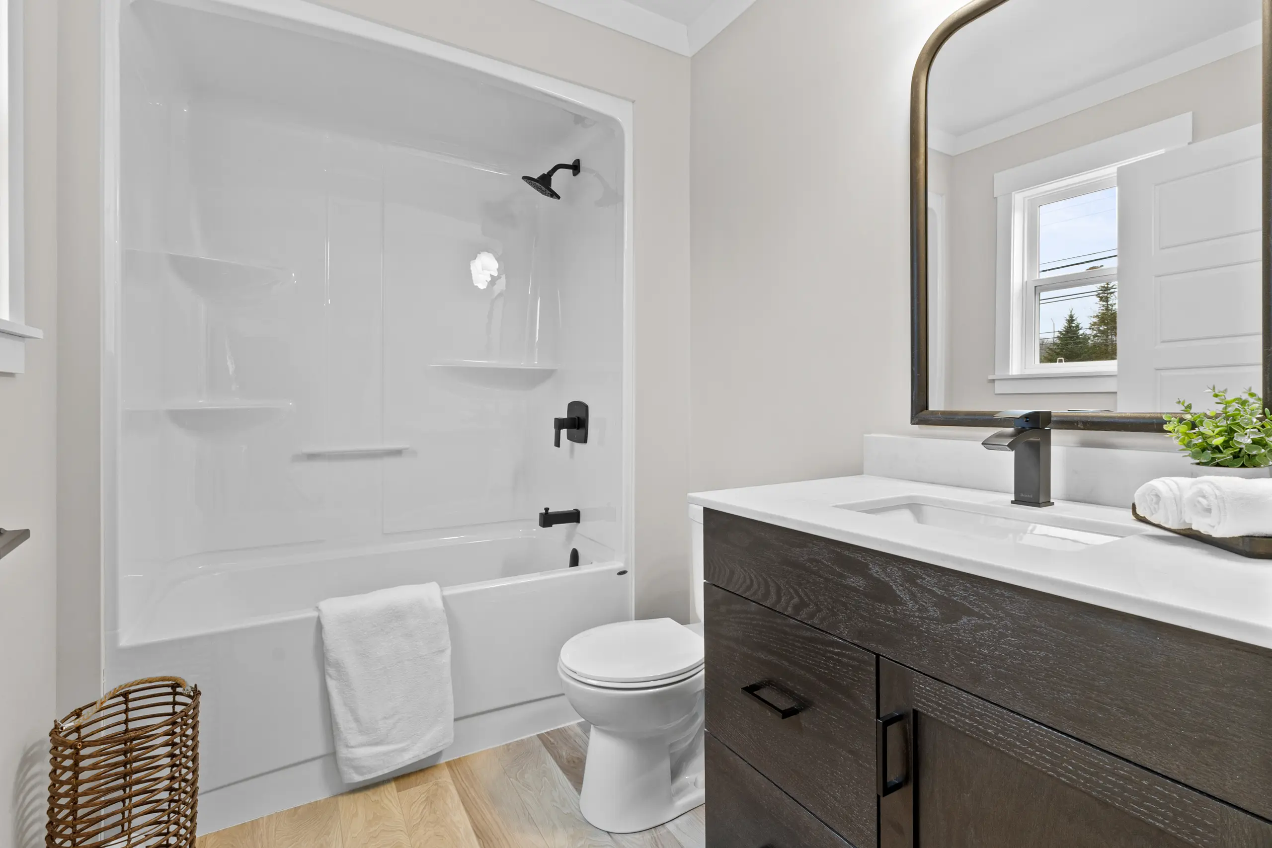 Contemporary bathroom featuring a dark wood vanity, large framed mirror, white tub-shower combination, and modern black fixtures. 