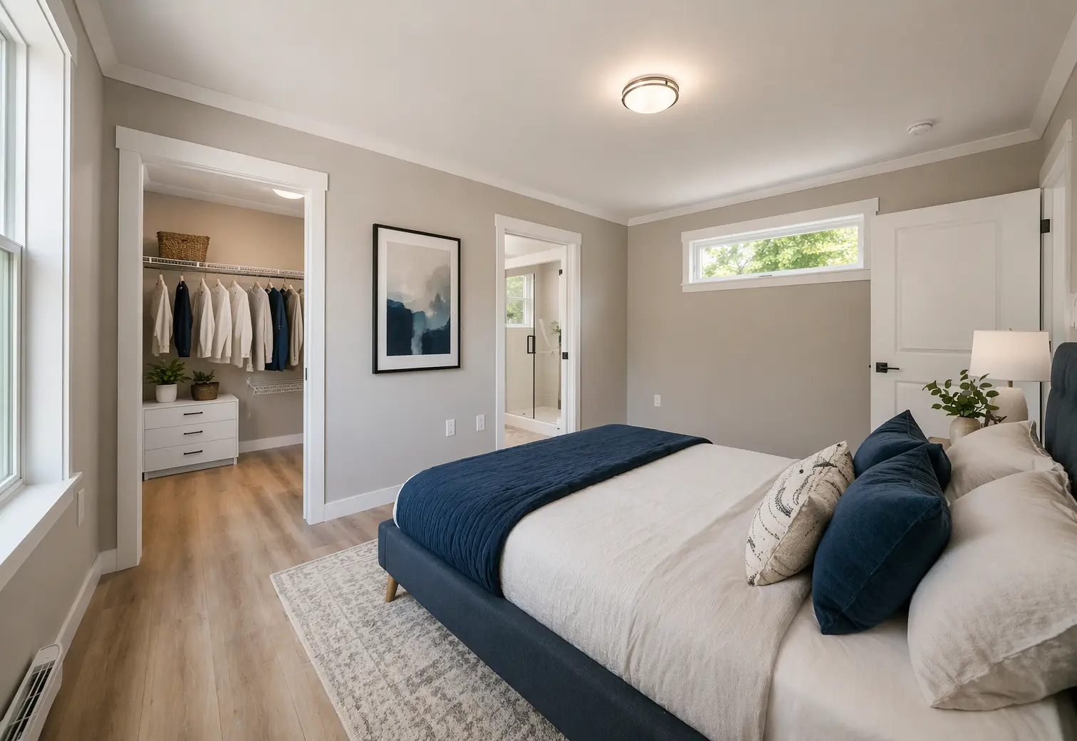Serene primary bedroom featuring a blue upholstered bed, walk-in closet, ensuite access, and soft neutral finishes throughout. 
