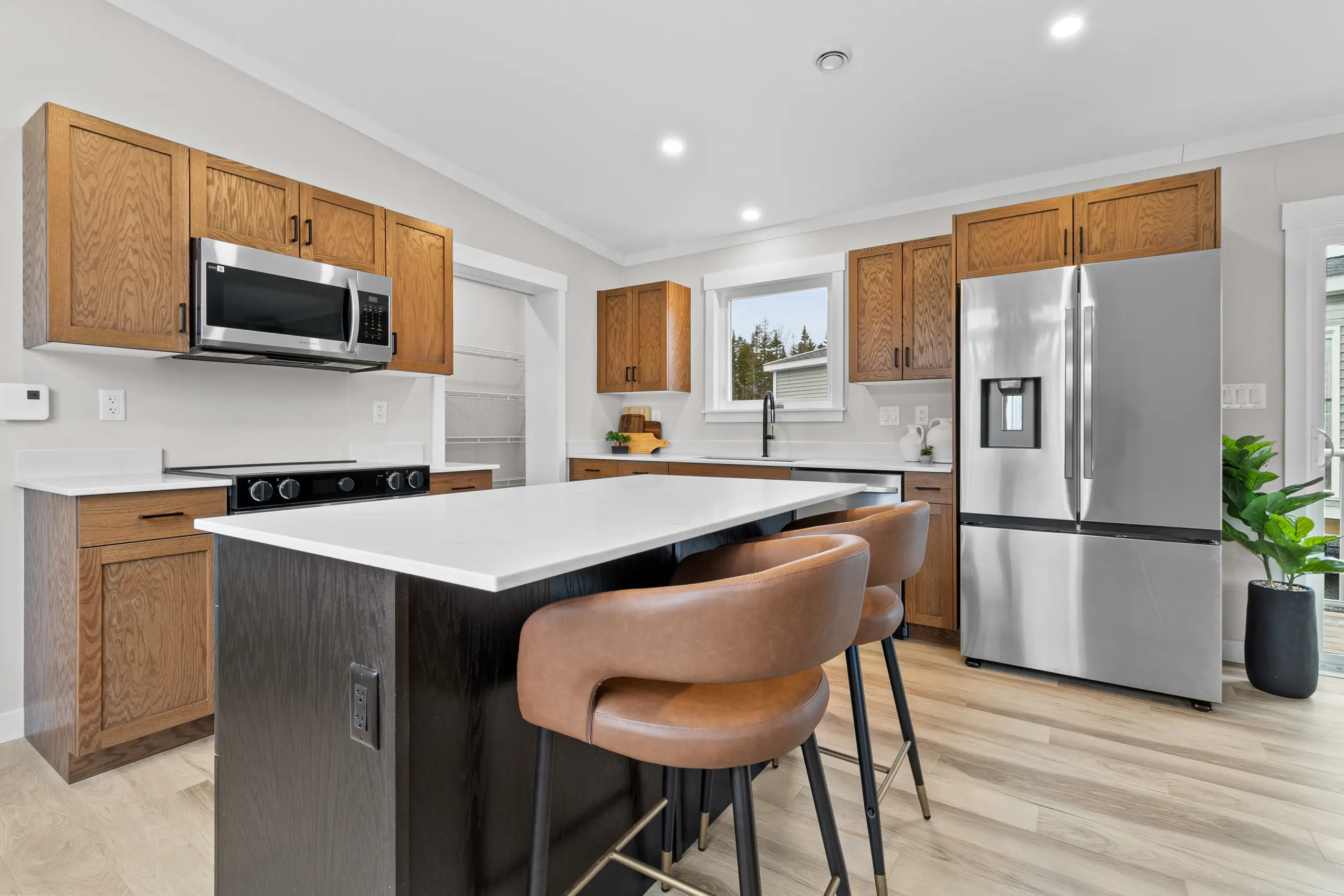 Modern kitchen with warm wood cabinetry, a large island with seating, stainless steel appliances, and a walk-in pantry. 