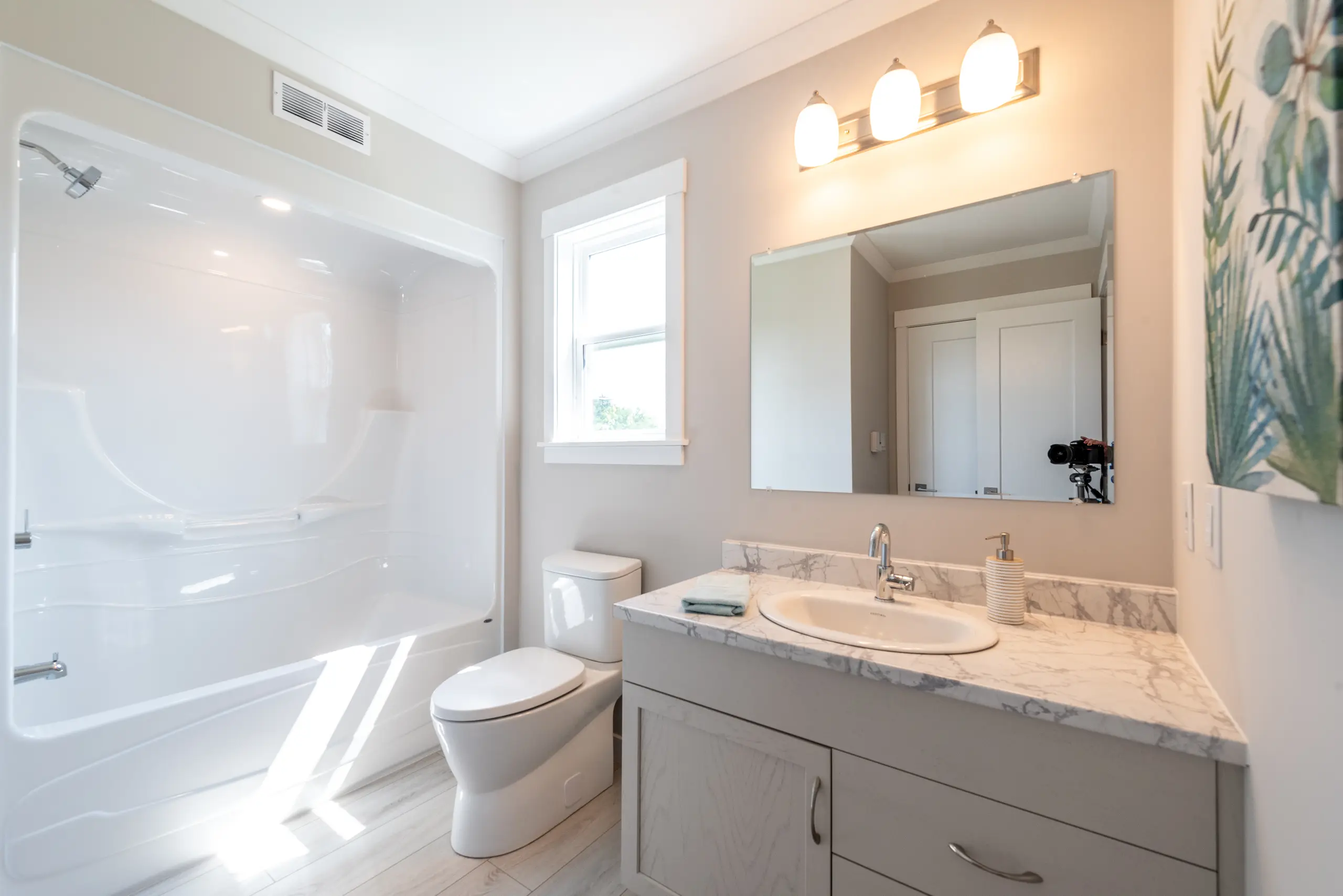 Bright bathroom with a tub and shower combination, large vanity, and natural light from a window.