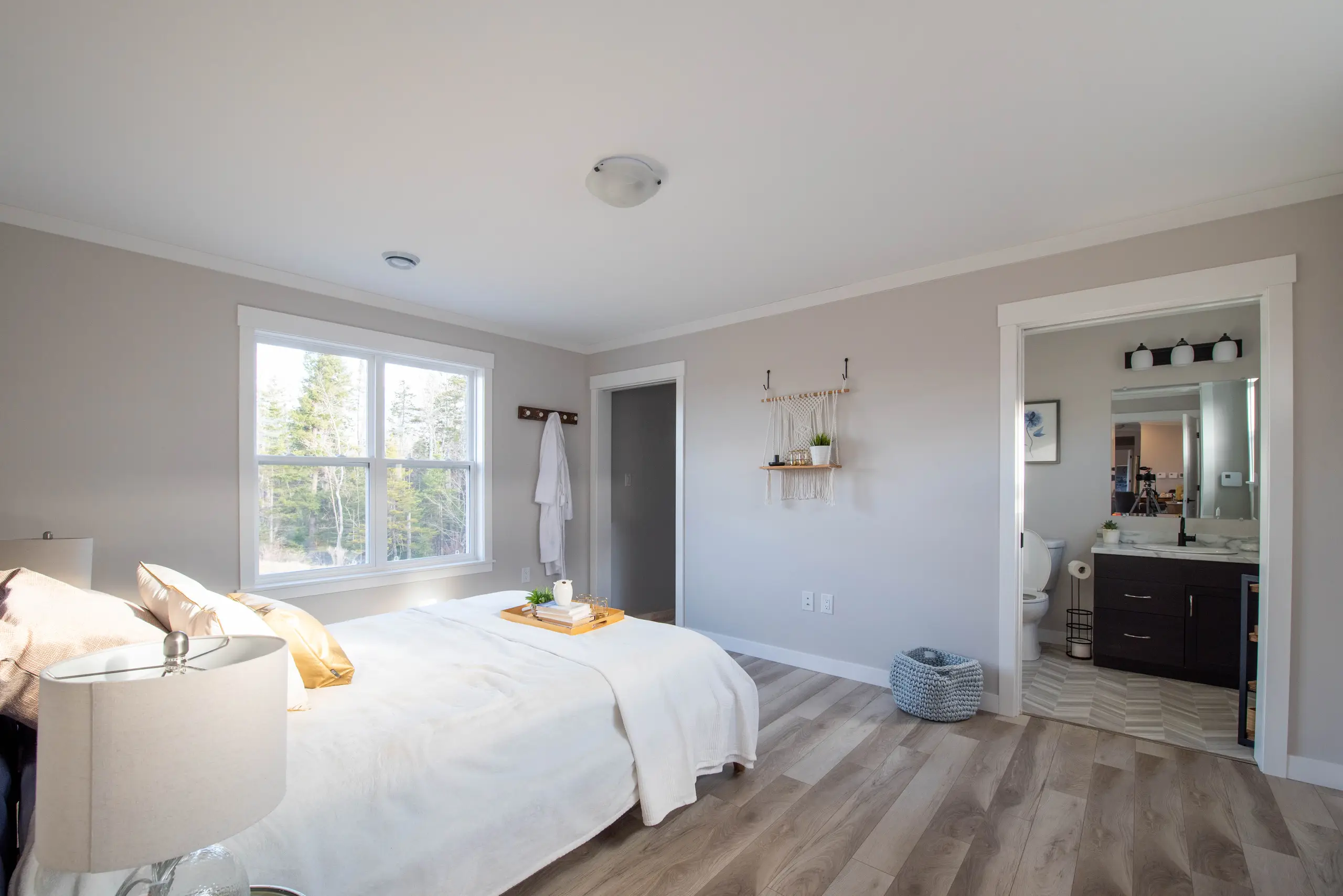 Bright primary bedroom featuring a large window, neutral finishes, a walk-in closet, and an ensuite bathroom with a dark wood vanity. 
